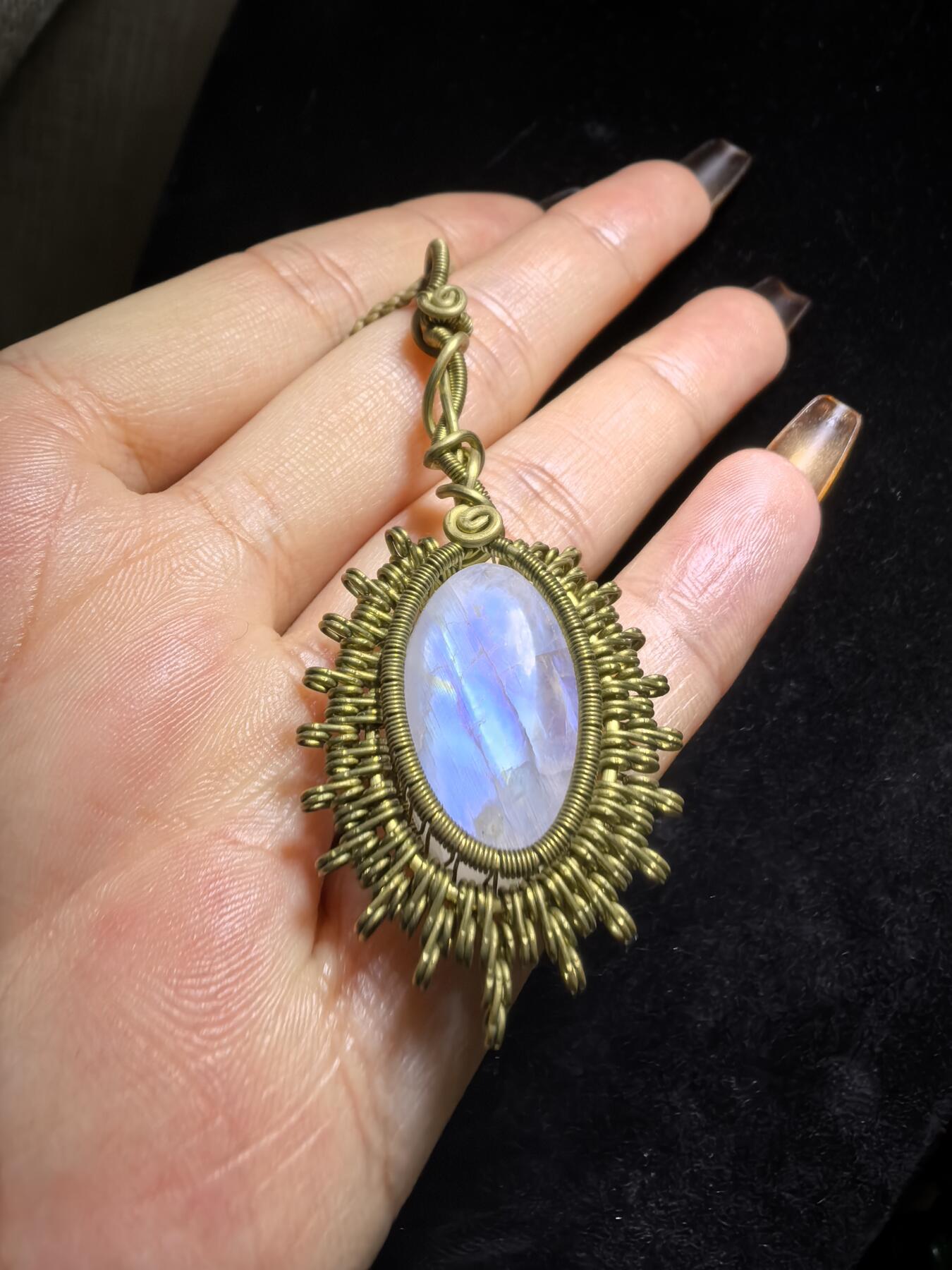 来自委内瑞拉国际友人手工绕丝工艺，月光石吊坠 从不同角度观察，它展现出不同的色彩魅力。有时是极光般的梦幻色彩，有时是少女般的温柔色彩，还有时是落日晚霞般的绚烂色彩。 佩戴与众不同独一无二。 尺寸:2.9cm*2.6cm*1.9cm ​