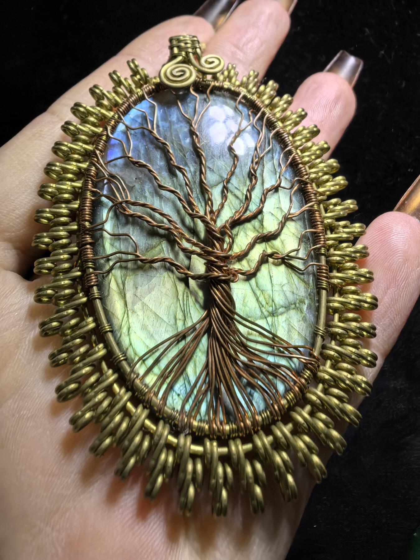 委内瑞拉国际友人纯手工绕丝工艺《灵光生命之树吊坠》男女款
以铜线手工编织的生命之树坐落在蓝火拉布拉多长石之上，整件作品带来更强的净化与守护能量。采用巴西编绳，可自由调节长度。
一件汇聚光、根与灵性的护符。
​尺寸：7.1cm*5.1cm*0.8cm每一款都是独一无二，非量产。
​天然有机宝石内部无法避免结构纹理等，介意勿扰！