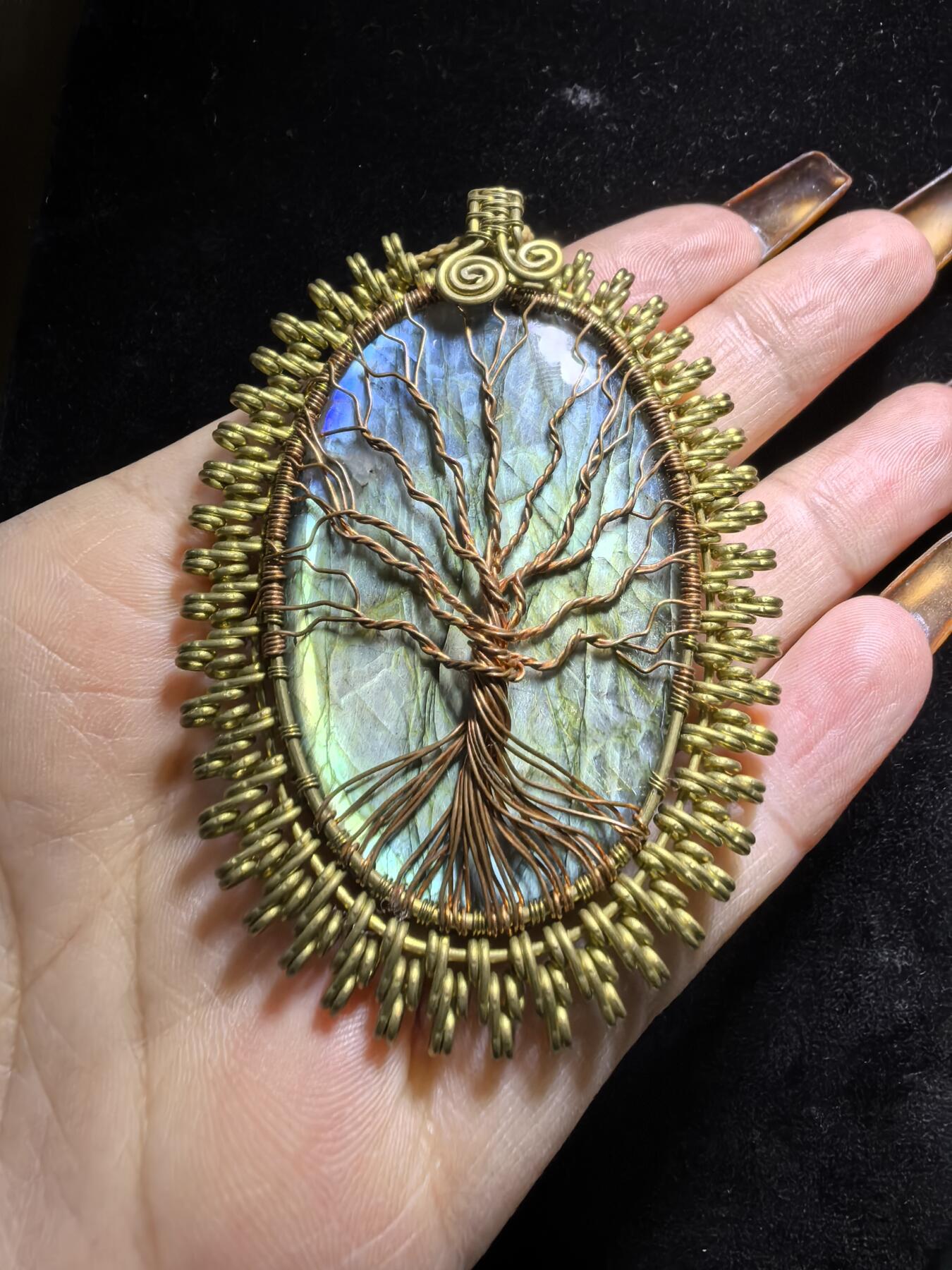 委内瑞拉国际友人纯手工绕丝工艺《灵光生命之树吊坠》男女款
以铜线手工编织的生命之树坐落在蓝火拉布拉多长石之上，整件作品带来更强的净化与守护能量。采用巴西编绳，可自由调节长度。
一件汇聚光、根与灵性的护符。
​尺寸：7.1cm*5.1cm*0.8cm每一款都是独一无二，非量产。
​天然有机宝石内部无法避免结构纹理等，介意勿扰！