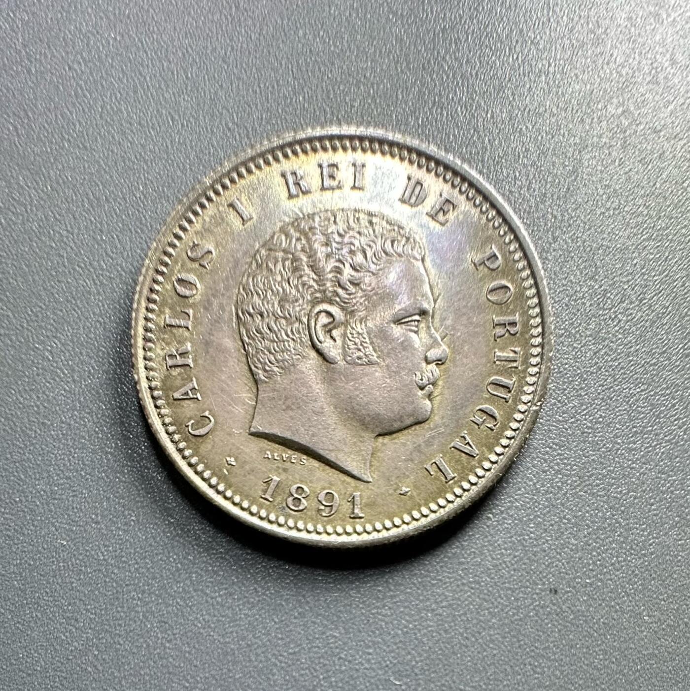 葡萄牙王国1891年200瑞斯的银币
	●	肖像与人物：
币面是卡洛斯一世（Carlos I）的侧面像（葡萄牙国王，1889 - 1908年在位），肖像风格体现19世纪末欧洲王室钱币的写实艺术特征。
	●	铭文与背景：
环绕葡萄牙文“CARLOS I REI DE PORTUGAL”（大意为“卡洛斯一世，葡萄牙国王”），明确君主身份与国家属性；下方“1891” 是铸造年份，“ALVES” 是雕刻师的名字（负责钱币肖像的模具雕刻）。
	●	材质与形制：圆形形制，边缘有珠纹装饰，工艺规整。