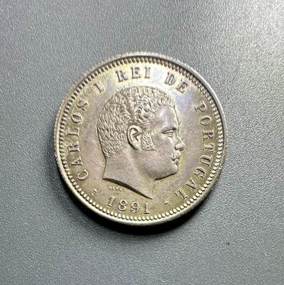 葡萄牙王国1891年200瑞斯的银币
	●	肖像与人物：
币面是卡洛斯一世（Carlos I）的侧面像（葡萄牙国王，1889 - 1908年在位），肖像风格体现19世纪末欧洲王室钱币的写实艺术特征。
	●	铭文与背景：
环绕葡萄牙文“CARLOS I REI DE PORTUGAL”（大意为“卡洛斯一世，葡萄牙国王”），明确君主身份与国家属性；下方“1891” 是铸造年份，“ALVES” 是雕刻师的名字（负责钱币肖像的模具雕刻）。
	●	材质与形制：圆形形制，边缘有珠纹装饰，工艺规整。