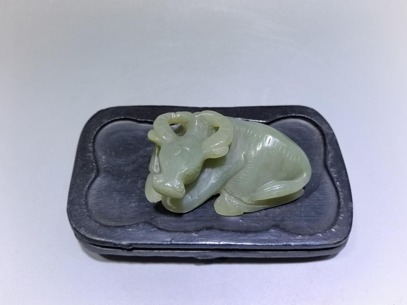 旧藏和田青白玉卧牛镇纸，传世雅物。
玉质青润细腻，包浆醇厚自然，雕工娴熟流畅，卧牛造型憨态可掬，栩栩如生。
牛角弯转，神态悠然，肌理线条精准传神，尽显古玉之韵与匠人之心。
既是文房镇纸，亦是案头雅赏，承载着“牛气冲天、扭转乾坤”的美好寓意，为藏家不可多得的臻品。5.5cm＊3.6cm＊2.0cm
克重：53.2g