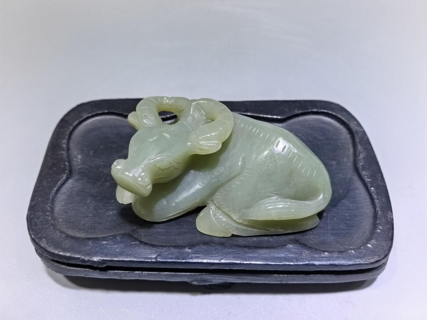 旧藏和田青白玉卧牛镇纸，传世雅物。
玉质青润细腻，包浆醇厚自然，雕工娴熟流畅，卧牛造型憨态可掬，栩栩如生。
牛角弯转，神态悠然，肌理线条精准传神，尽显古玉之韵与匠人之心。
既是文房镇纸，亦是案头雅赏，承载着“牛气冲天、扭转乾坤”的美好寓意，为藏家不可多得的臻品。5.5cm＊3.6cm＊2.0cm
克重：53.2g