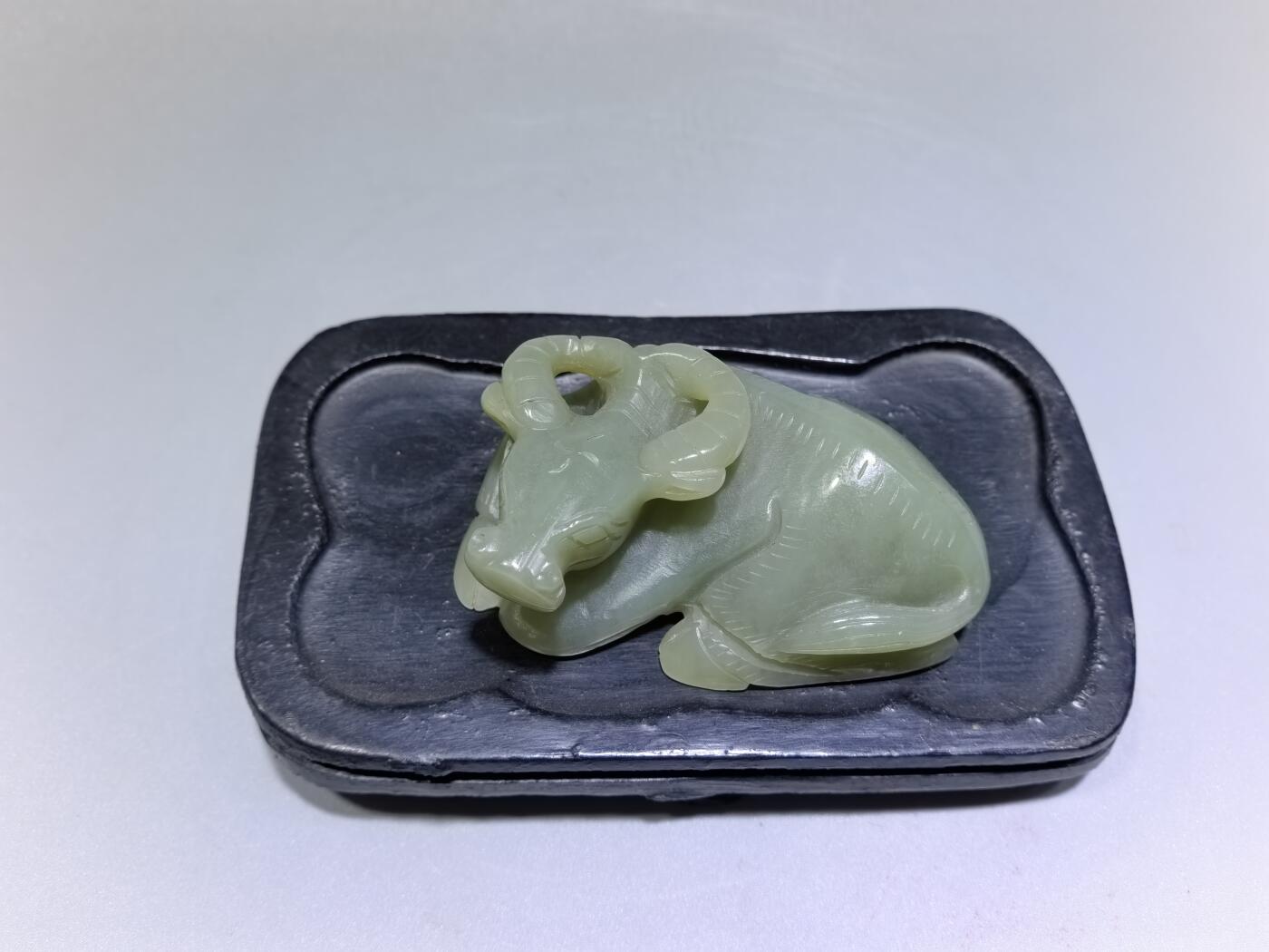 旧藏和田青白玉卧牛镇纸，传世雅物。
玉质青润细腻，包浆醇厚自然，雕工娴熟流畅，卧牛造型憨态可掬，栩栩如生。
牛角弯转，神态悠然，肌理线条精准传神，尽显古玉之韵与匠人之心。
既是文房镇纸，亦是案头雅赏，承载着“牛气冲天、扭转乾坤”的美好寓意，为藏家不可多得的臻品。5.5cm＊3.6cm＊2.0cm
克重：53.2g