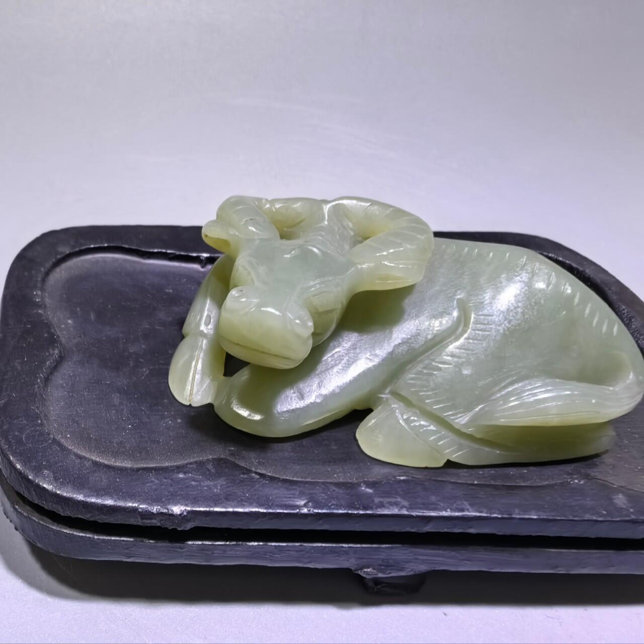 旧藏和田青白玉卧牛镇纸，传世雅物。
玉质青润细腻，包浆醇厚自然，雕工娴熟流畅，卧牛造型憨态可掬，栩栩如生。
牛角弯转，神态悠然，肌理线条精准传神，尽显古玉之韵与匠人之心。
既是文房镇纸，亦是案头雅赏，承载着“牛气冲天、扭转乾坤”的美好寓意，为藏家不可多得的臻品。5.5cm＊3.6cm＊2.0cm
克重：53.2g