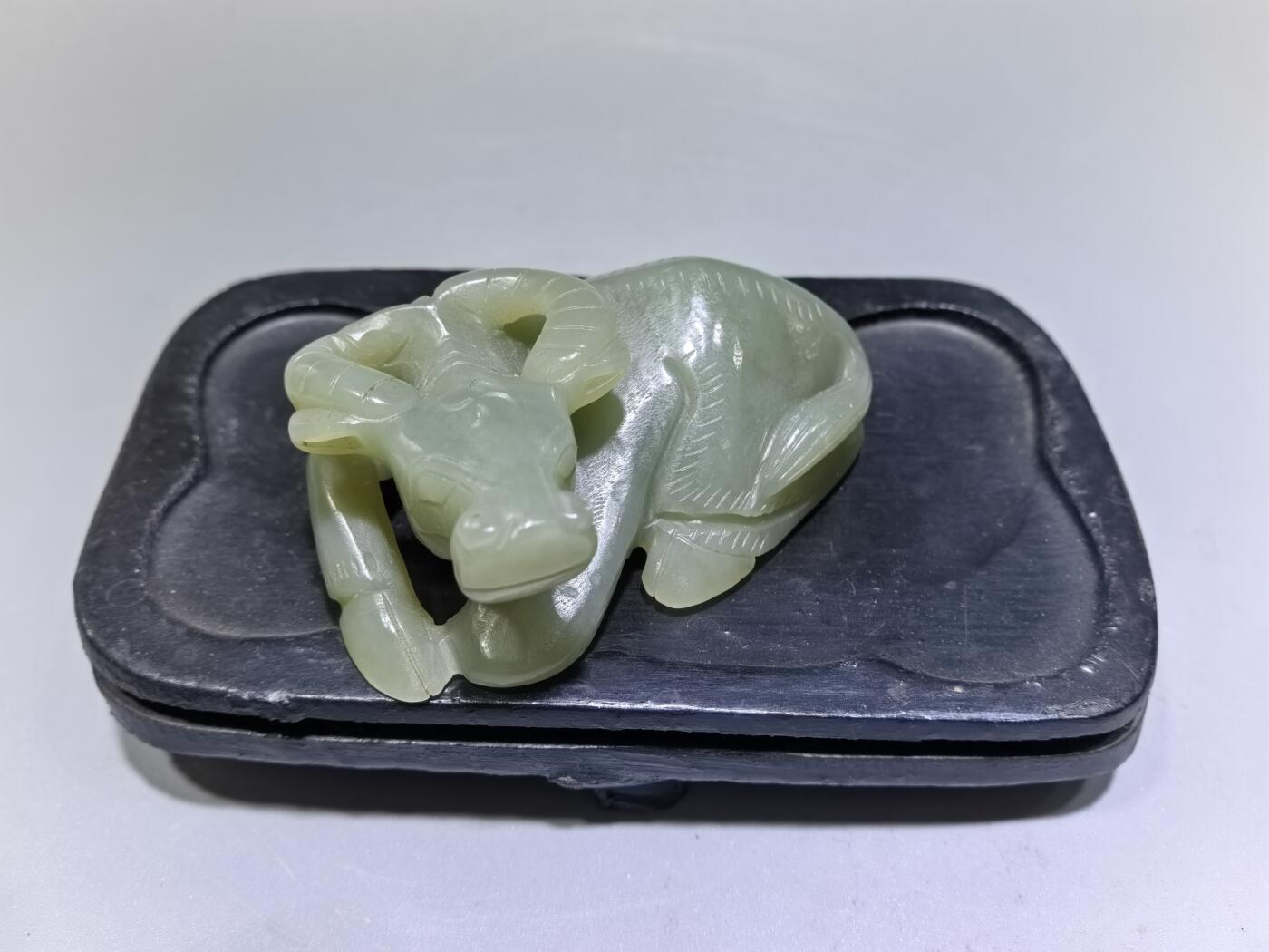 旧藏和田青白玉卧牛镇纸，传世雅物。
玉质青润细腻，包浆醇厚自然，雕工娴熟流畅，卧牛造型憨态可掬，栩栩如生。
牛角弯转，神态悠然，肌理线条精准传神，尽显古玉之韵与匠人之心。
既是文房镇纸，亦是案头雅赏，承载着“牛气冲天、扭转乾坤”的美好寓意，为藏家不可多得的臻品。5.5cm＊3.6cm＊2.0cm
克重：53.2g
