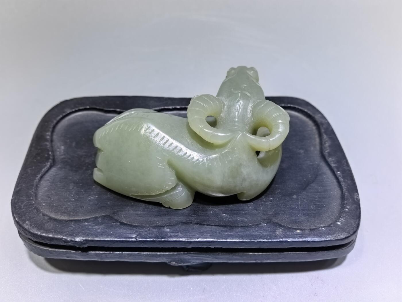 旧藏和田青白玉卧牛镇纸，传世雅物。
玉质青润细腻，包浆醇厚自然，雕工娴熟流畅，卧牛造型憨态可掬，栩栩如生。
牛角弯转，神态悠然，肌理线条精准传神，尽显古玉之韵与匠人之心。
既是文房镇纸，亦是案头雅赏，承载着“牛气冲天、扭转乾坤”的美好寓意，为藏家不可多得的臻品。5.5cm＊3.6cm＊2.0cm
克重：53.2g