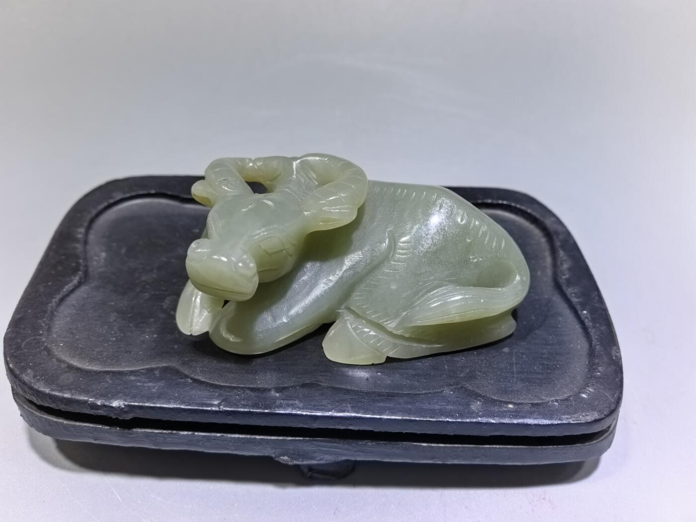 旧藏和田青白玉卧牛镇纸，传世雅物。
玉质青润细腻，包浆醇厚自然，雕工娴熟流畅，卧牛造型憨态可掬，栩栩如生。
牛角弯转，神态悠然，肌理线条精准传神，尽显古玉之韵与匠人之心。
既是文房镇纸，亦是案头雅赏，承载着“牛气冲天、扭转乾坤”的美好寓意，为藏家不可多得的臻品。5.5cm＊3.6cm＊2.0cm
克重：53.2g