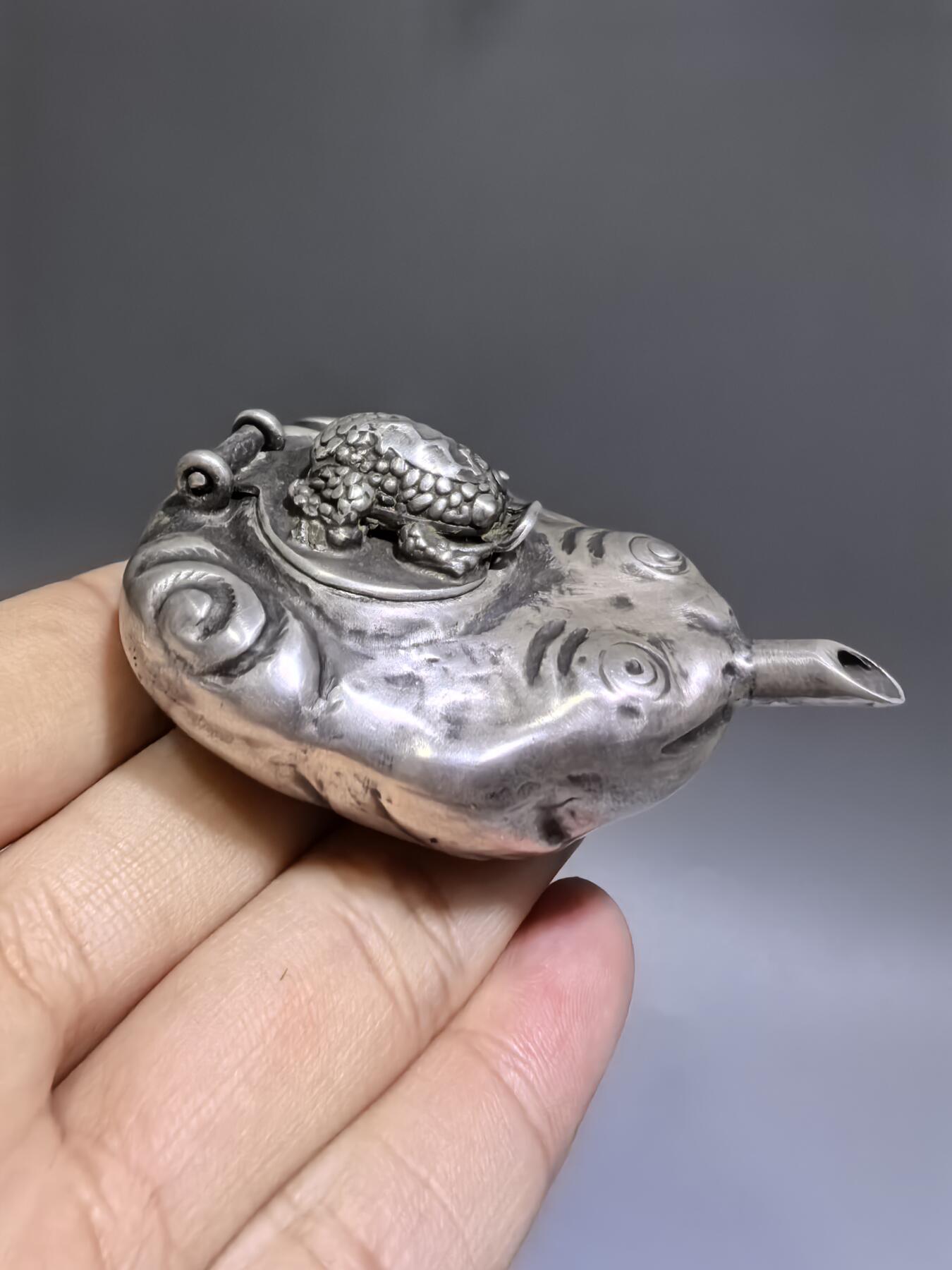 老银金蟾砚滴案头纳福墨韵生清代·老银金蟾纹砚滴材质：足银工艺：手工锻打、高浮雕錾刻器型：随形砚滴，云纹为底，金蟾为钮，壶嘴精巧品相：传世美品，包浆醇厚，工艺精湛金蟾为传统招财瑞兽，此砚滴以银为材，将瑞兽与文房雅器结合，既具实用价值，又含吉祥寓意，是清代银制文房的精品之作极具收藏与赏玩价值​6.3cm*4.0cm*2.8cm克重：24g#砚滴#清代#老银