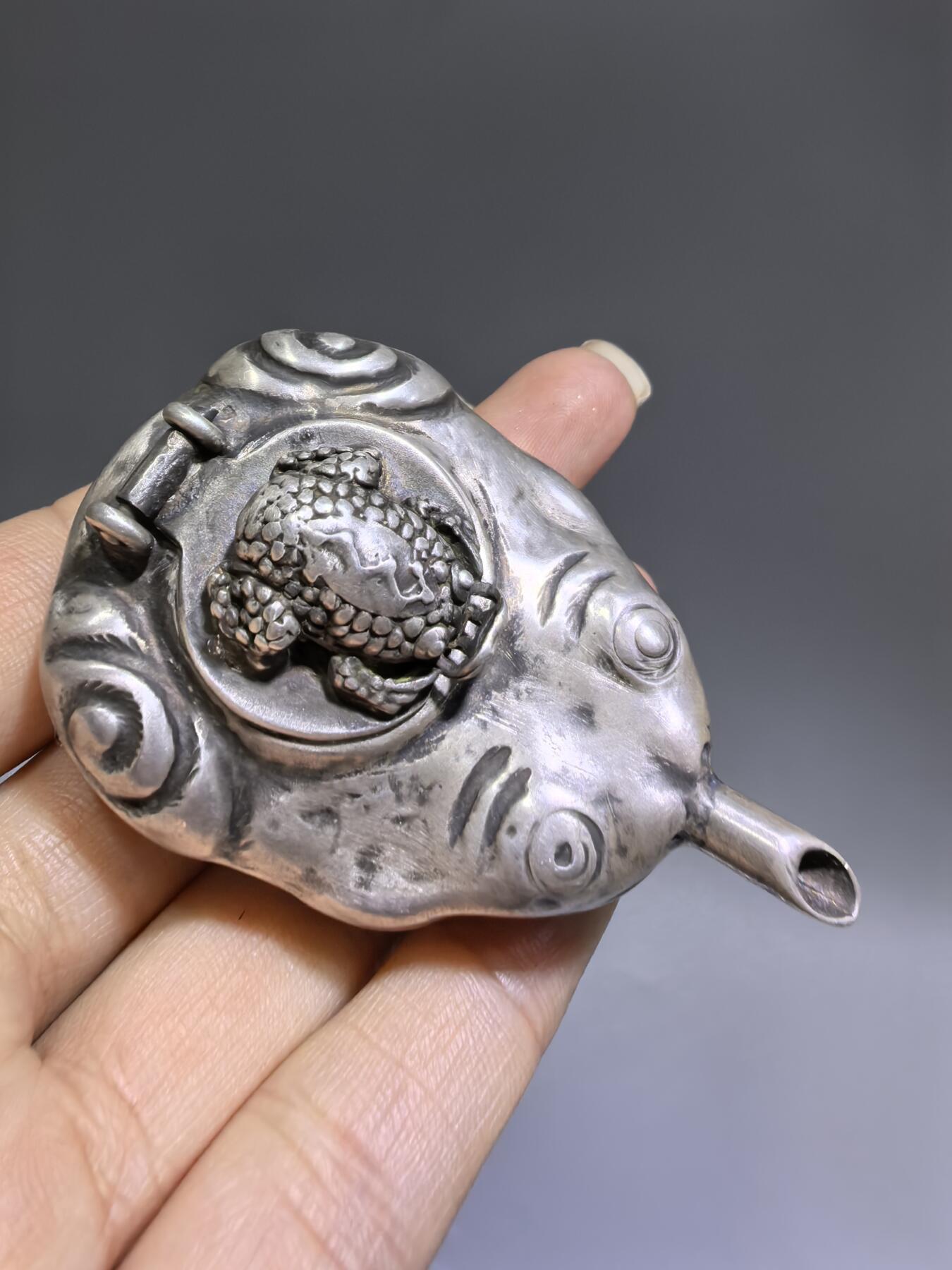 老银金蟾砚滴案头纳福墨韵生清代·老银金蟾纹砚滴材质：足银工艺：手工锻打、高浮雕錾刻器型：随形砚滴，云纹为底，金蟾为钮，壶嘴精巧品相：传世美品，包浆醇厚，工艺精湛金蟾为传统招财瑞兽，此砚滴以银为材，将瑞兽与文房雅器结合，既具实用价值，又含吉祥寓意，是清代银制文房的精品之作极具收藏与赏玩价值​6.3cm*4.0cm*2.8cm克重：24g#砚滴#清代#老银