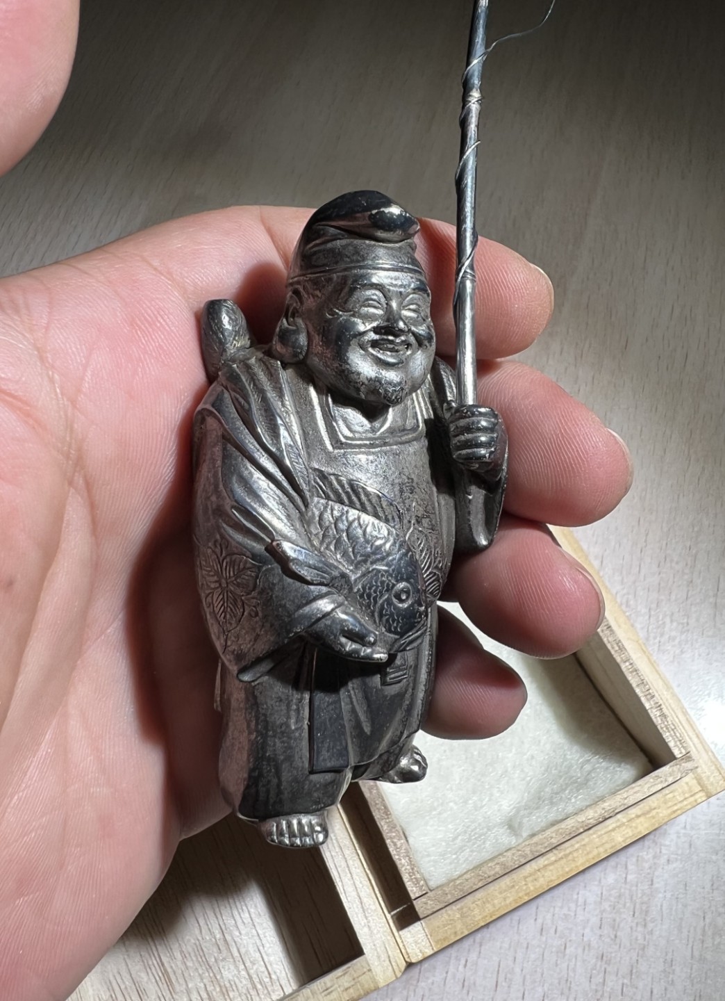 大猫徽章拍卖第205期 纯银财神惠比须摆件，附原木盒，证书 惠比须（亦称惠比寿、夷，日语：えびす）是日本神话中的海神，属于七福神之一，也是七福神中唯一一个日本固有神明。常见的形象是头戴乌帽子、身穿狩衣、右手持钓竿、左手抱鲷鱼的姿态。惠比须是原先是日本渔民信仰的海上守护神，后来由于海运的兴起而成了商业神、财神，到14、15世纪演变为了全日本民众信仰的财神、商业神。日本著名金工，佐野宏行，号宏采，制作。