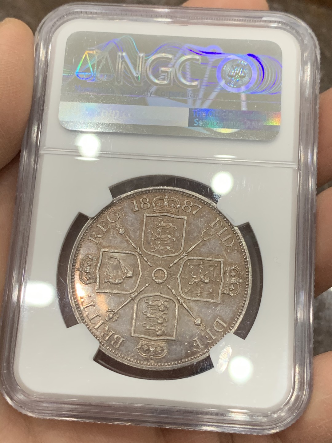 《竞宝斋》第128场-周日，周一 ，2场连拍（全场包邮） NGC-MS63 英国1887年高冠双佛洛林银币，比较少的罗马数字版本，双面呈镜面效果，包浆颜色也是很好看的淡粉彩，上手非常的好看，值得收藏