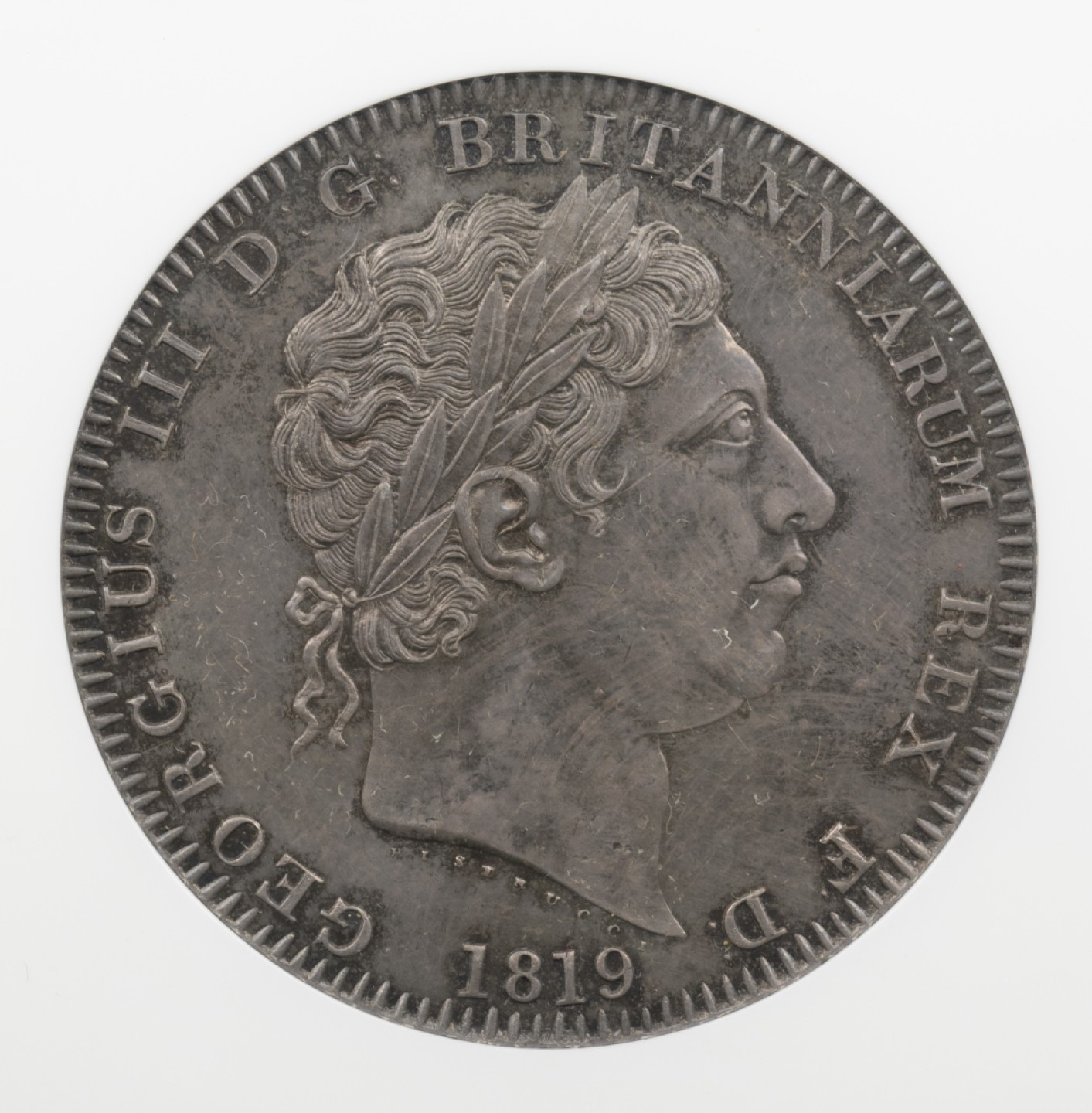 万国钱币拍卖第005期 1819LIX英国乔治三世马剑银币，英国马剑系列的开端，机制克朗的鼻祖，也代表着蒸汽时代的到来。马剑图案由意大利雕刻家Pistrucci设计，在钱币两面皆留下了显而易见的签名，这在当时是难以被接受的（一般只会留下首字母缩写），此举也为后来首席雕刻师W.Wyon的上位埋下了伏笔。此枚钱币高点细节皆属完美，略带镜面感的底板在光线下呈现出五彩斑斓的色彩，整体状态有着不输64分的水准。