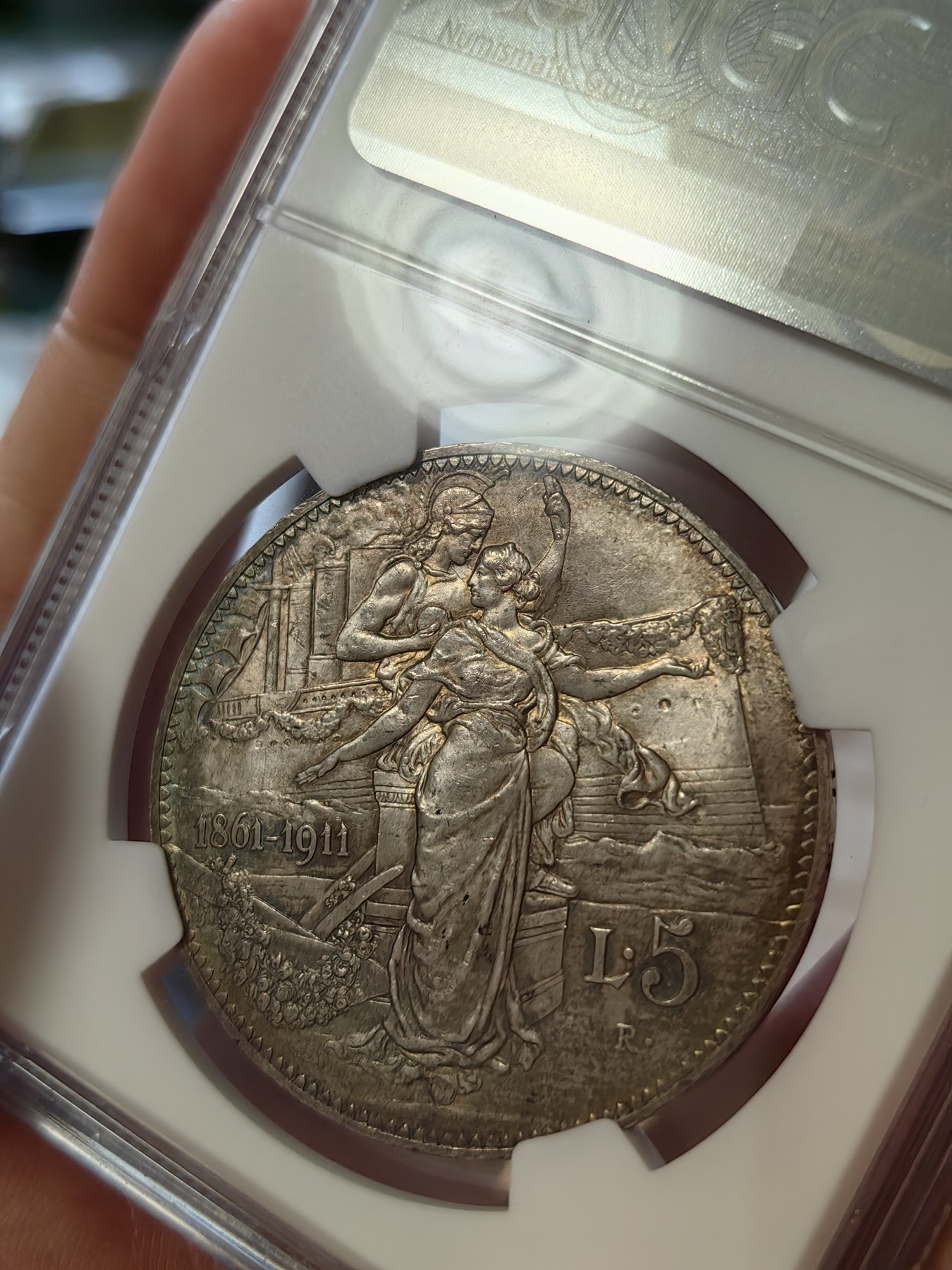 橡树集藏-006场 海纳百川 ngc-ms64 1911年意大利建国5里拉大银币 打制优异 浮雕完好 整体状态相当不错 币圈大托奶  罗马厂内部评选最美设计 正面为埃马努埃莱三世，意大利国王。背面图案为代表古罗马的士兵和代表现代意大利的女神，以及象征工农业繁荣的轮船、犁铧和花环。背面情景指的是古罗马向现代罗马——意大利递送地球，象征治世权力的传承～币的边铭，刻有双环八字结，代表爱的意思，萨伏伊王室常用。