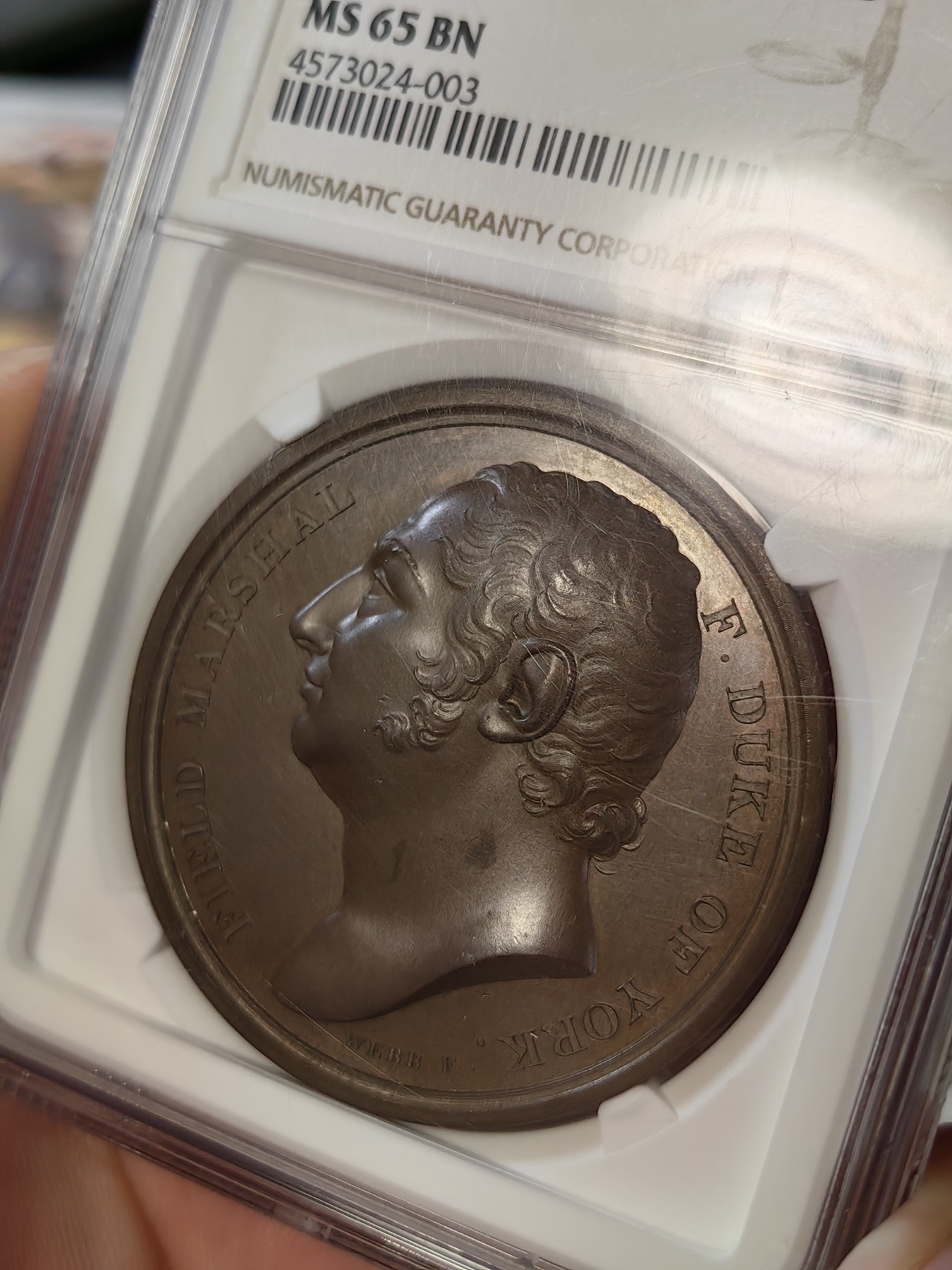 橡树集藏-006场 海纳百川 1813年英国皇室章，乔治三世时期原铸。ngc Ms65，加厚盒。铜色诱人，镜面感十足。背面是女王向皇家近卫军团授予军旗，细节丰富，雕刻精细，超高浮雕。ngc数据库唯一评级，冠军分。军旗上刻字：VIRES ACQUIRT EUNDO。拉丁文，意为“随行聚力”，是古罗马诗人的叙事诗《埃涅阿斯纪》中的一句，意思是“随着传播而越来越有力”。象征着军队听从指挥，雷厉风行。