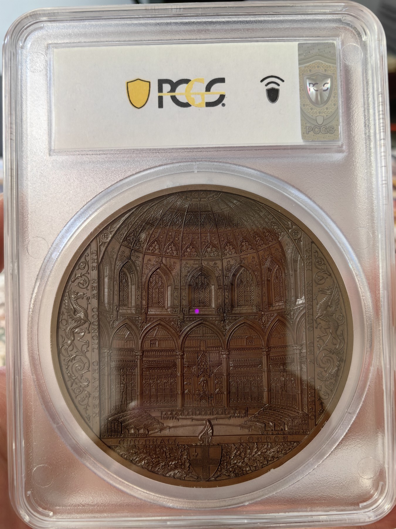 橡树集藏-006场 海纳百川 pcgs-sp67！ 1884年英国伦敦金融城系列 大不列颠市政厅铜牌新议会厅开幕，伦敦造币厂。作者：JS & AB Wyon。直径：77毫米。正面：伦迪尼亚，商业和治安法官出席，向她的议会发表讲话；背面：市政厅内景。这种高度复杂的反向设计显示出令人难以置信的雄伟，是任何大教堂和建筑相关奖牌的高级收藏者的必备品。丰富的红棕色表面，具有巨大的光泽度，令人叹为观止。附带原盒，插销损坏。