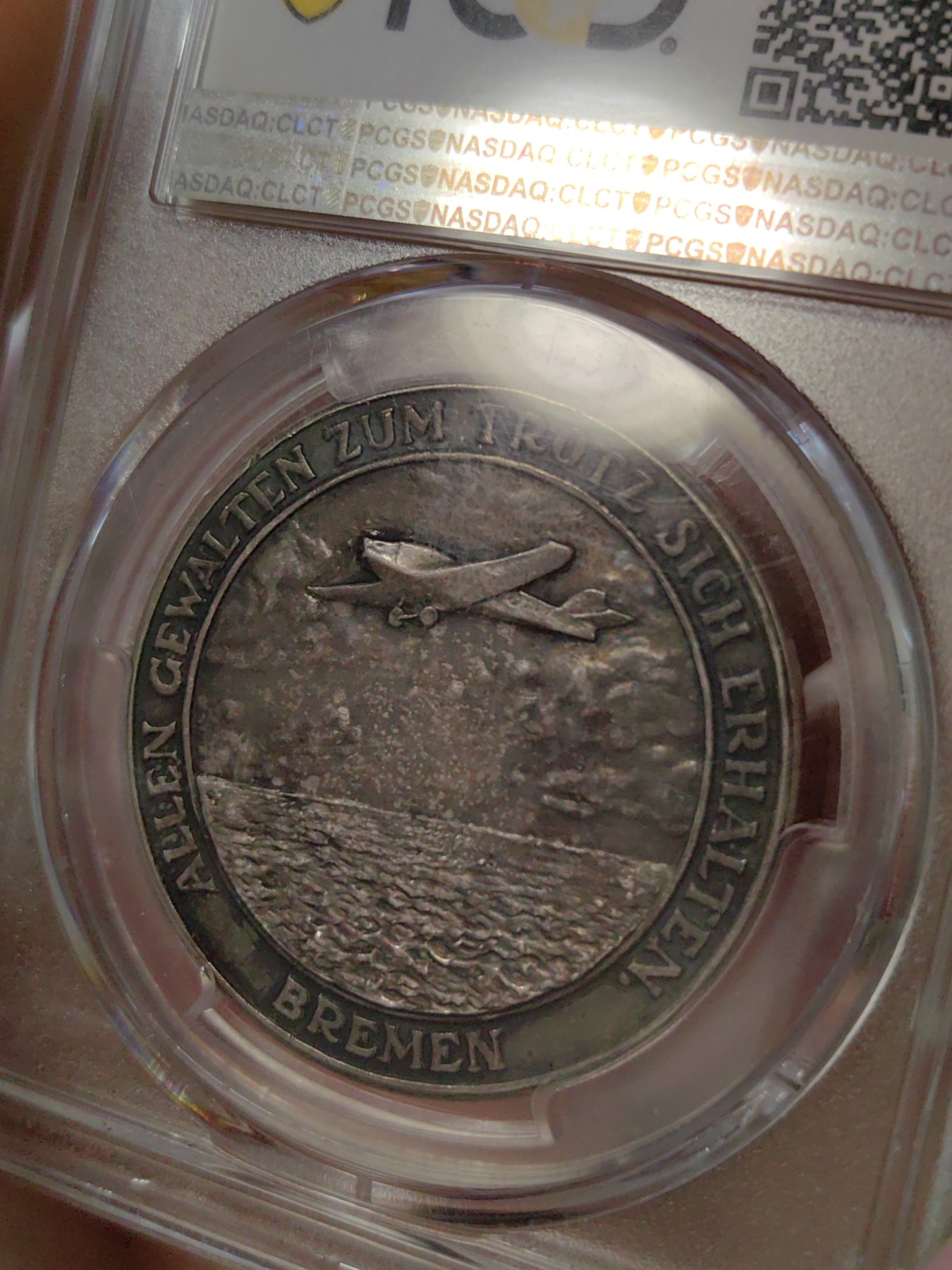 橡树集藏-006场 海纳百川 1928年德国银章，pcgs SP63。纪念不莱梅号飞机飞越大西洋。1928年4月13日，两名德国飞行员驾驶飞机在美国费城着陆，这是人类首次驾驶飞机从大西洋东岸飞到西岸。这两名飞行员在费城受到了盛大欢迎，德国人也以他们为傲，发行 多枚以此事件为主题的纪念章。 双面浓郁包浆，五彩，超高浮雕，实物极美。 人物刻画精细，背面的不莱梅号穿过云雾，飞翔在大西洋上空，海面波光粼粼，惟妙惟肖。