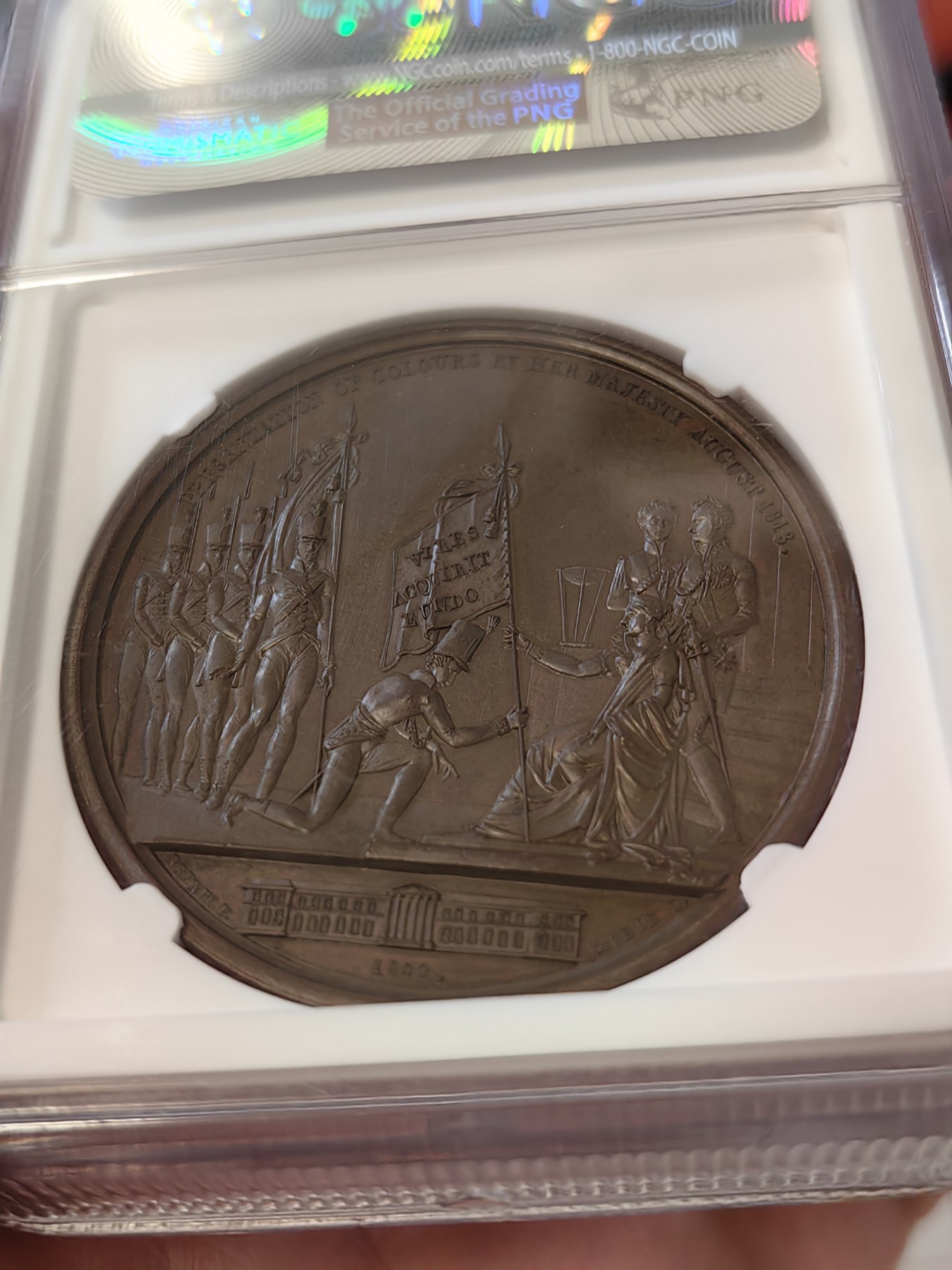 橡树集藏-006场 海纳百川 1813年英国皇室章，乔治三世时期原铸。ngc Ms65，加厚盒。铜色诱人，镜面感十足。背面是女王向皇家近卫军团授予军旗，细节丰富，雕刻精细，超高浮雕。ngc数据库唯一评级，冠军分。军旗上刻字：VIRES ACQUIRT EUNDO。拉丁文，意为“随行聚力”，是古罗马诗人的叙事诗《埃涅阿斯纪》中的一句，意思是“随着传播而越来越有力”。象征着军队听从指挥，雷厉风行。