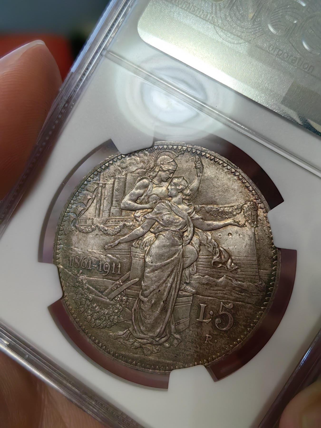 橡树集藏-006场 海纳百川 ngc-ms64 1911年意大利建国5里拉大银币 打制优异 浮雕完好 整体状态相当不错 币圈大托奶  罗马厂内部评选最美设计 正面为埃马努埃莱三世，意大利国王。背面图案为代表古罗马的士兵和代表现代意大利的女神，以及象征工农业繁荣的轮船、犁铧和花环。背面情景指的是古罗马向现代罗马——意大利递送地球，象征治世权力的传承～币的边铭，刻有双环八字结，代表爱的意思，萨伏伊王室常用。