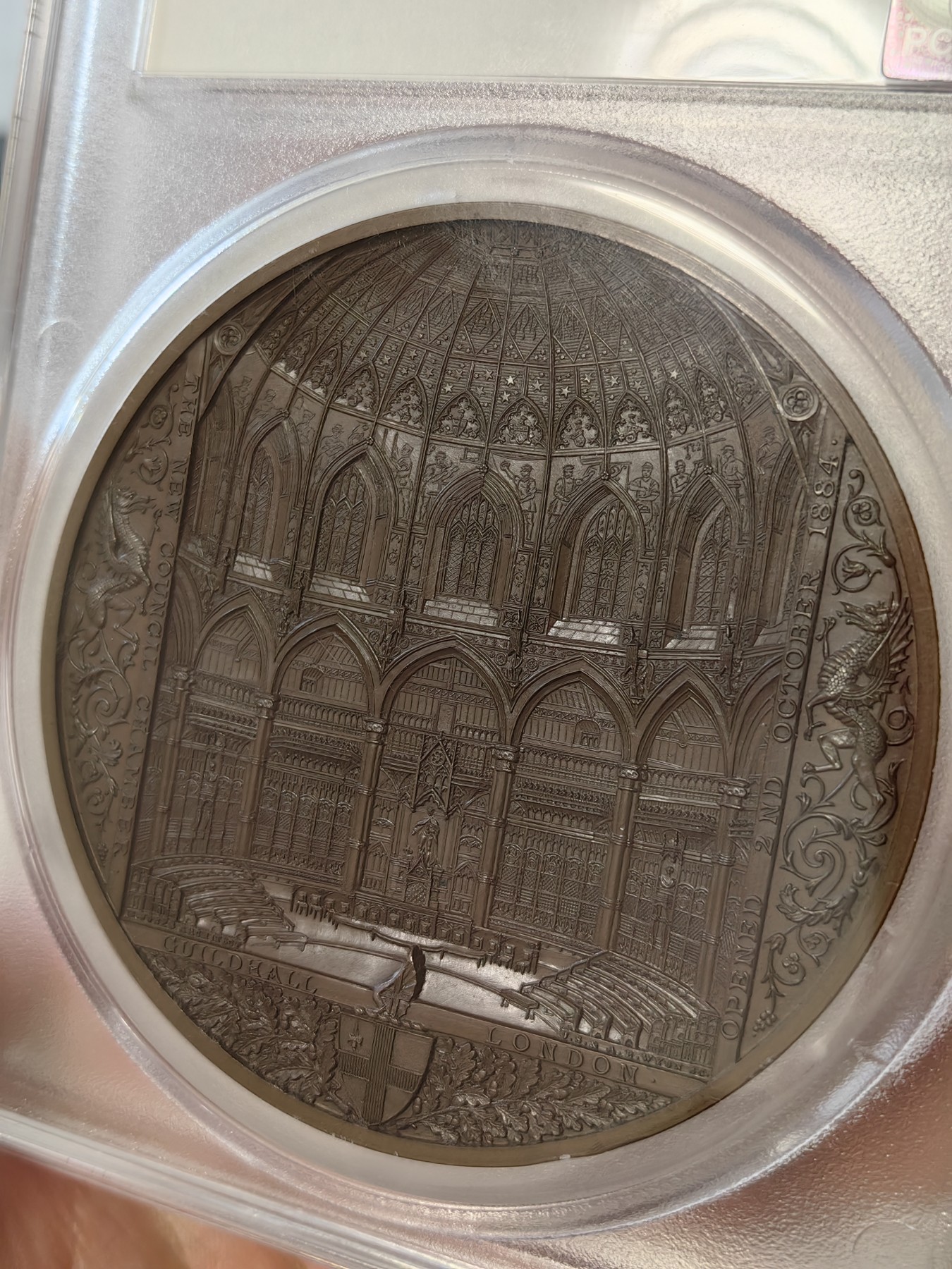 橡树集藏-006场 海纳百川 pcgs-sp67！ 1884年英国伦敦金融城系列 大不列颠市政厅铜牌新议会厅开幕，伦敦造币厂。作者：JS & AB Wyon。直径：77毫米。正面：伦迪尼亚，商业和治安法官出席，向她的议会发表讲话；背面：市政厅内景。这种高度复杂的反向设计显示出令人难以置信的雄伟，是任何大教堂和建筑相关奖牌的高级收藏者的必备品。丰富的红棕色表面，具有巨大的光泽度，令人叹为观止。附带原盒，插销损坏。