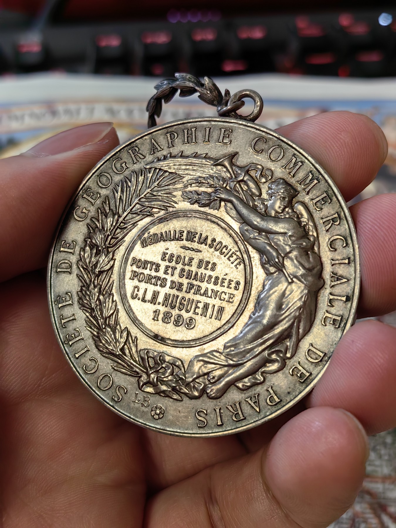 橡树集藏-006场 海纳百川 法国商业地理学会银奖章，1899 年。GEM 未流通。51毫米，58.92 克。作者：L.Botte。1899 年发行并赠送给卡米尔-莱昂-伊波利特·胡格南。正面：地理女神站在左侧，将月桂花环放在商业女神上，手持双杖；背景是商业和工业的标志，例如地球仪、敦、齿轮、铁砧、灯塔和船。完美出厂品相，高浮雕细节极佳，女神和天使柔美动人。