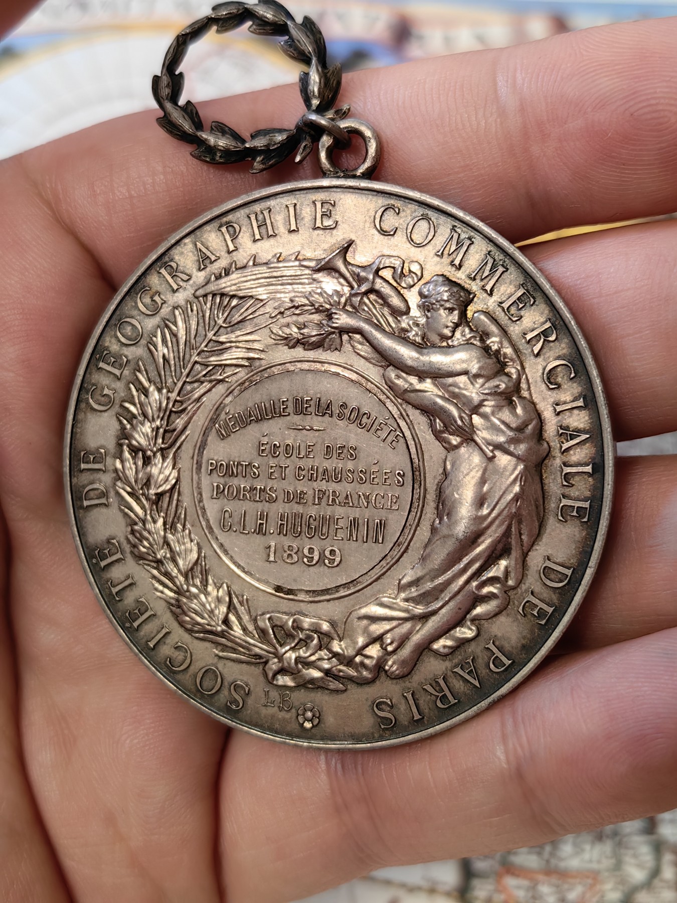 橡树集藏-006场 海纳百川 法国商业地理学会银奖章，1899 年。GEM 未流通。51毫米，58.92 克。作者：L.Botte。1899 年发行并赠送给卡米尔-莱昂-伊波利特·胡格南。正面：地理女神站在左侧，将月桂花环放在商业女神上，手持双杖；背景是商业和工业的标志，例如地球仪、敦、齿轮、铁砧、灯塔和船。完美出厂品相，高浮雕细节极佳，女神和天使柔美动人。