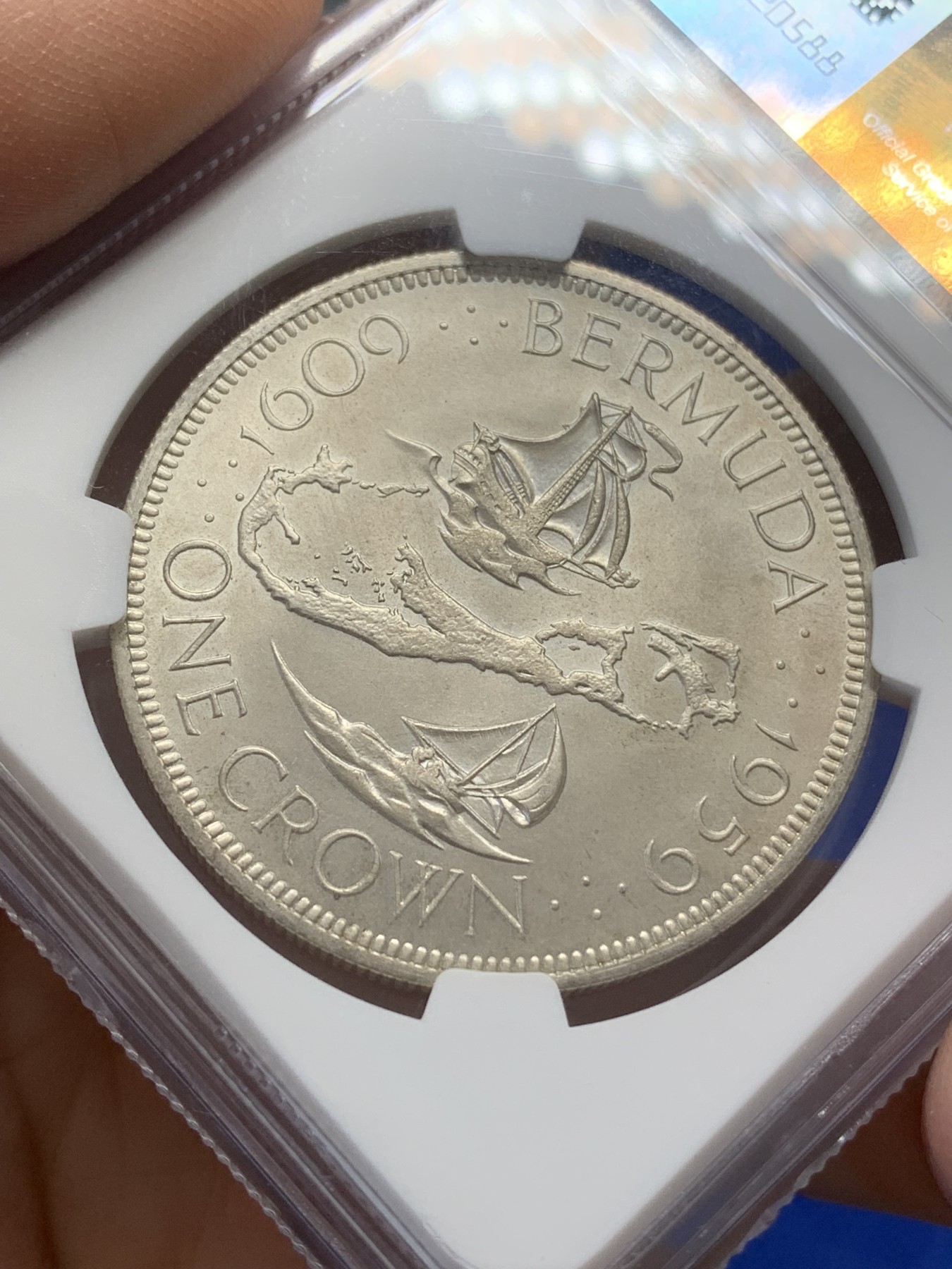 《竞宝斋》第218场-周日，周一 2场 (全场包邮) NGC-MS64 英属百慕大群岛1959年伊丽莎白二世1克朗银币，直径38mm，重28.28克，925银，发行量100010枚。自治的英国海外领地独立发行的首枚钱币。车轮转光，非常漂亮。