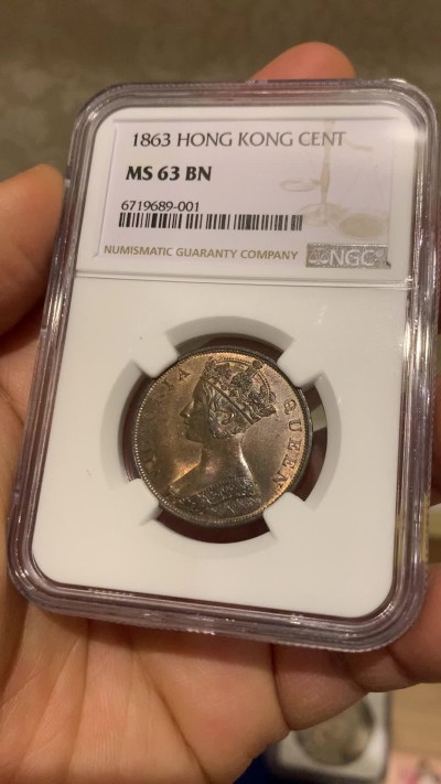 《竞宝斋》圣诞专辑  第一场  第227场 定制纪念章相赠 (全场顺丰包邮) NGC-MS63 香港1863年维多利亚女王香港一仙铜币。该品种流通币之首年，沿用了本土无神弗洛林的经典头像设计，背面是极具中国风味的文字排布，整币图案细腻文字工整，底板对光平滑，有一丝样币风范。以多点光源照射则光韵流畅盈满，辫子无常见弱打。巧克力色非常舒服，不输大多数64的状态，一步到位的东西。