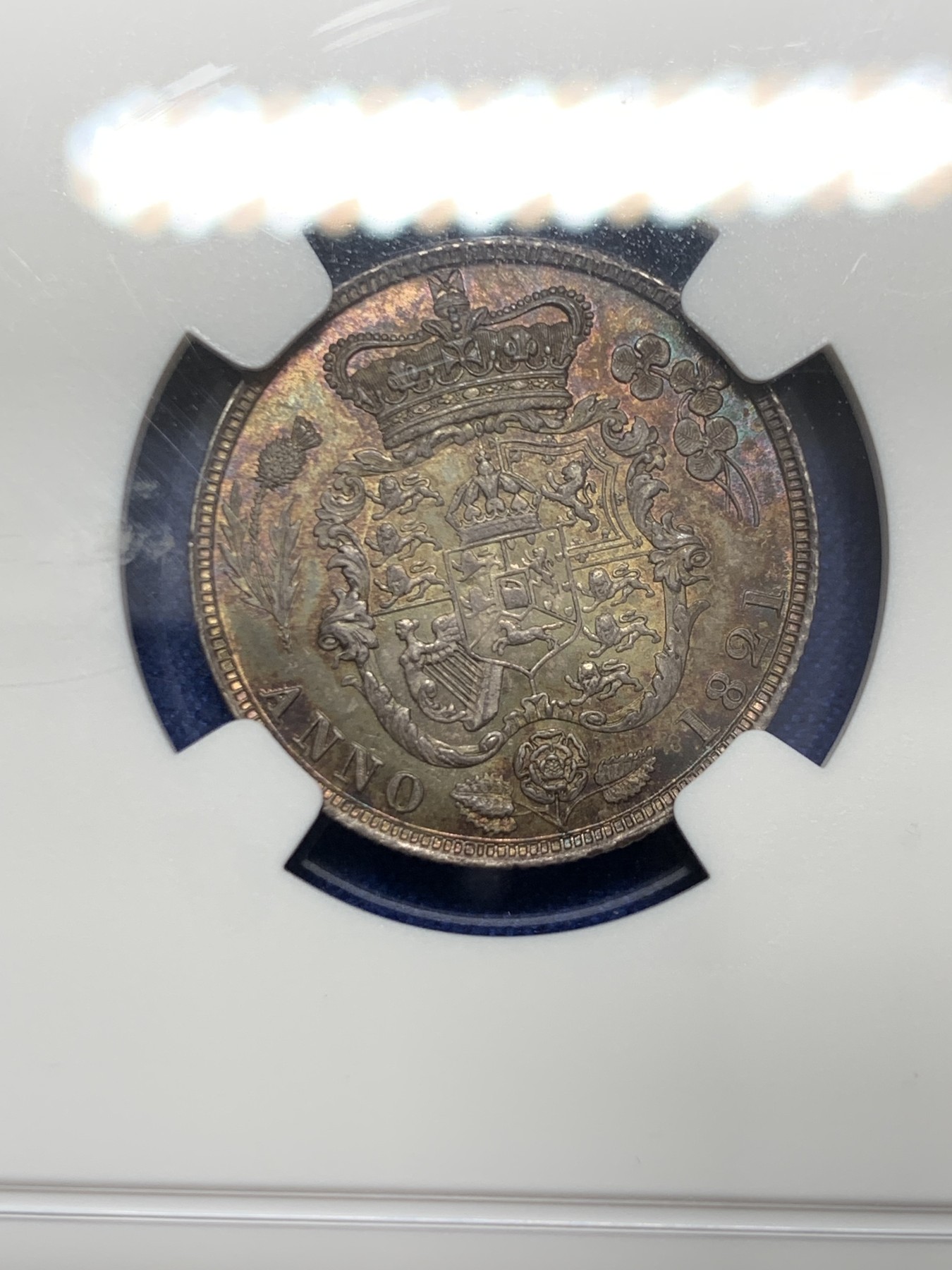 《竞宝斋》圣诞专辑  第二场  第228场 定制纪念章相赠 (全场顺丰包邮) NGC-MS66 英国1821年乔治四世1先令银币。币面环绕暖色系包浆，橘黄，红酒色，梅红，紫罗兰循序渐进。双面经典，正面头像来自皮斯特鲁奇；背面三花图案来自简·帕皮提斯特·梅林，签名隐藏在内齿。三叶草上暗记wwp为mint master的简拼。美国知名币商66+售价1850美金。