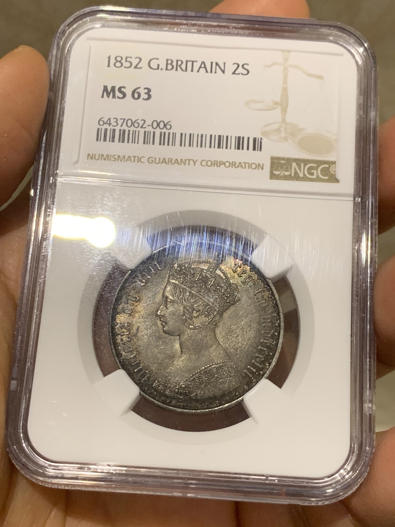 《竞宝斋》圣诞专辑  第二场  第228场 定制纪念章相赠 (全场顺丰包邮) NGC-MS63 英国1852年维多利亚女王哥特福林银币。正面包浆沉稳古气，但又能透出隐约的酒红光芒，背面是极其漂亮的五彩彩虹色过渡自然。这枚是整个系列的第一年，第一版女王面部线条和蔼柔美，值得入手。