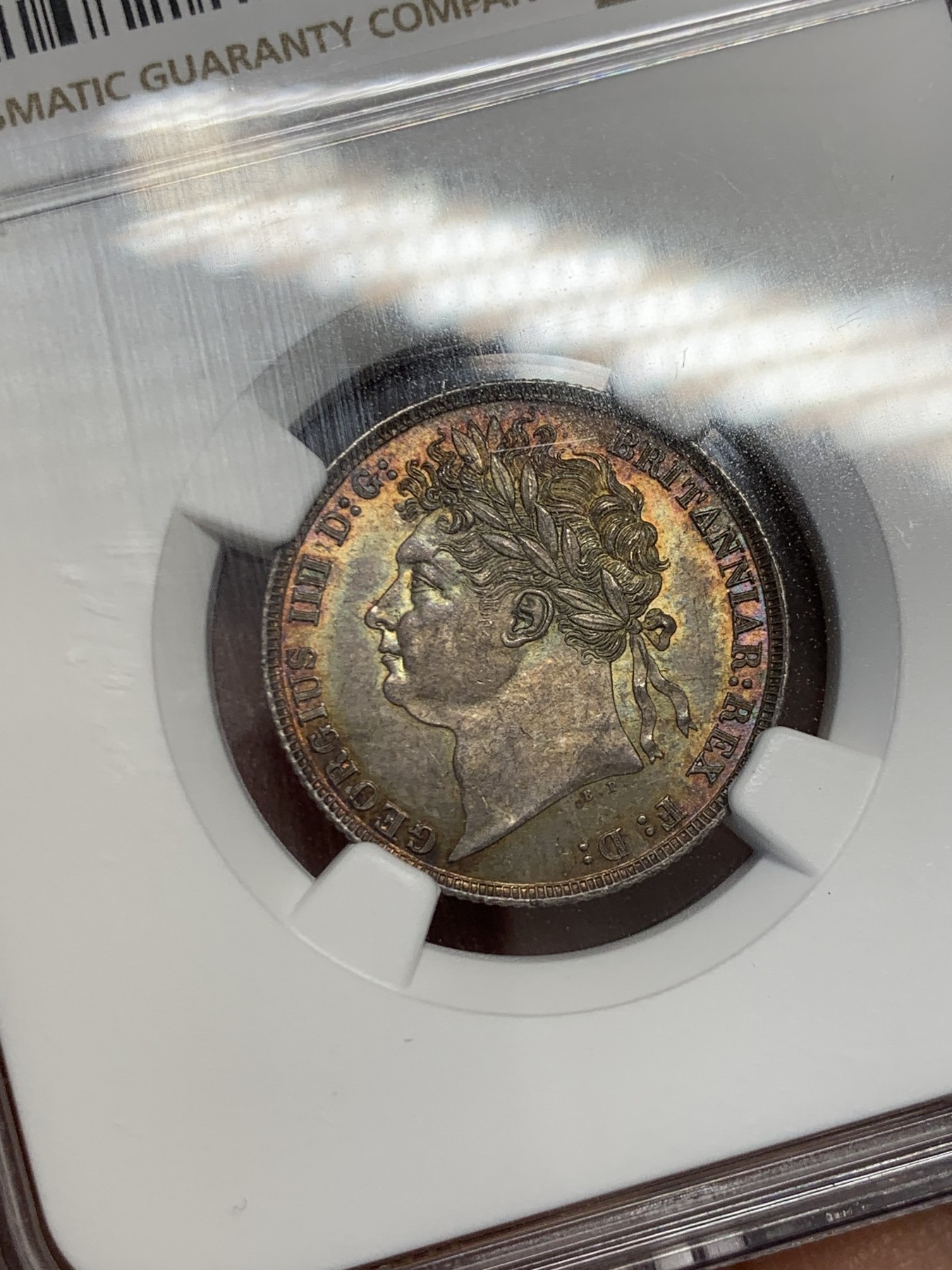 《竞宝斋》圣诞专辑  第二场  第228场 定制纪念章相赠 (全场顺丰包邮) NGC-MS66 英国1821年乔治四世1先令银币。币面环绕暖色系包浆，橘黄，红酒色，梅红，紫罗兰循序渐进。双面经典，正面头像来自皮斯特鲁奇；背面三花图案来自简·帕皮提斯特·梅林，签名隐藏在内齿。三叶草上暗记wwp为mint master的简拼。美国知名币商66+售价1850美金。