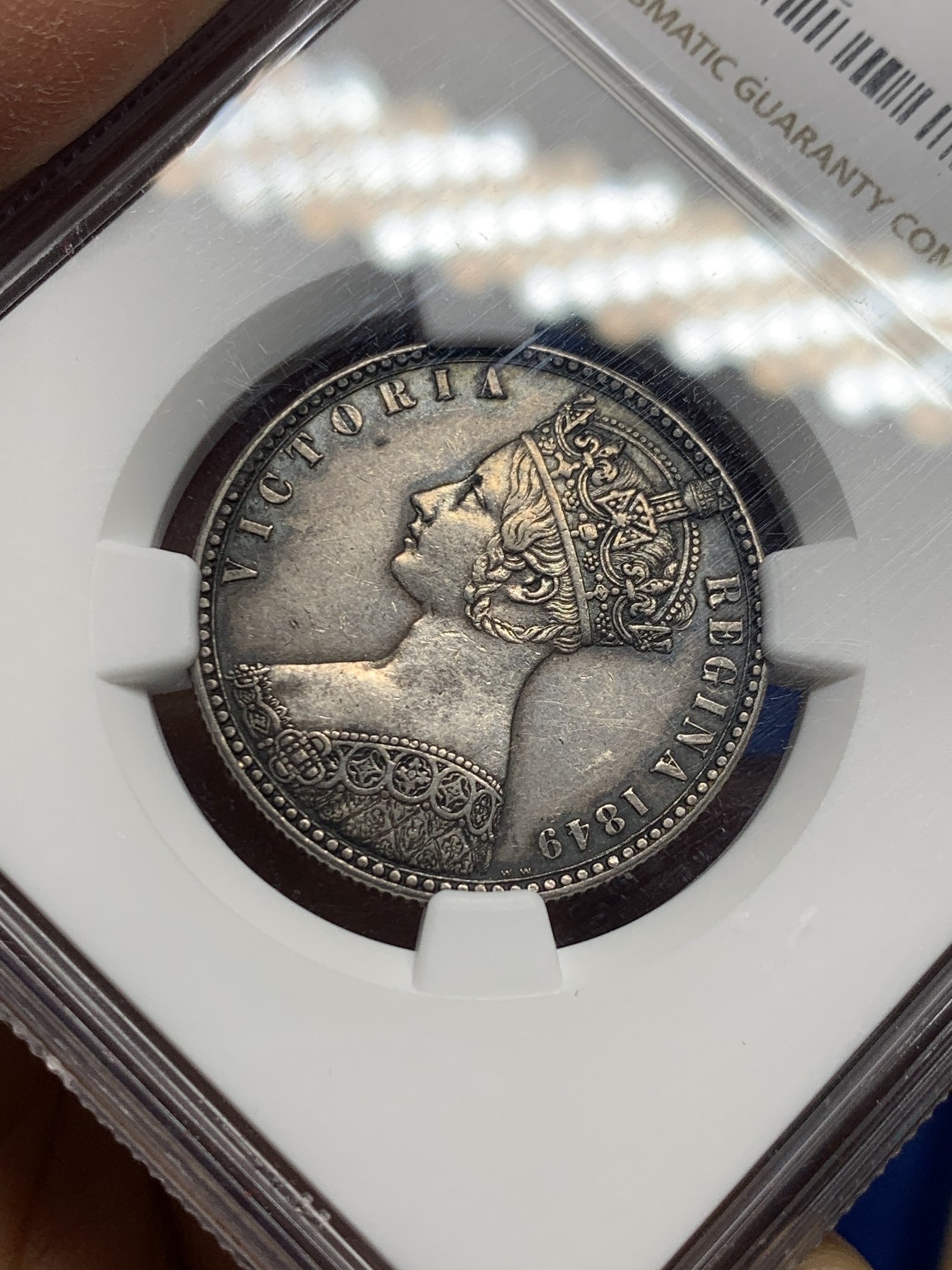 《竞宝斋》第240场-周日，周一 年终尾场 (全场包邮) NGC-AU55 英国1849年维多利亚无神弗洛林银币 英国第一枚弗洛林 第一枚没有D.G(君权神授) 正面是威廉怀恩作品 背面有代表英格兰、苏格兰、威尔士的三花 名誉品种 打制精美 五官皇冠服饰都清晰可见 特有的英系黑彩 钱币背后的故事丰富 只发行一年稀有（N家评级标签印成1949，难得的错误成了唯一）