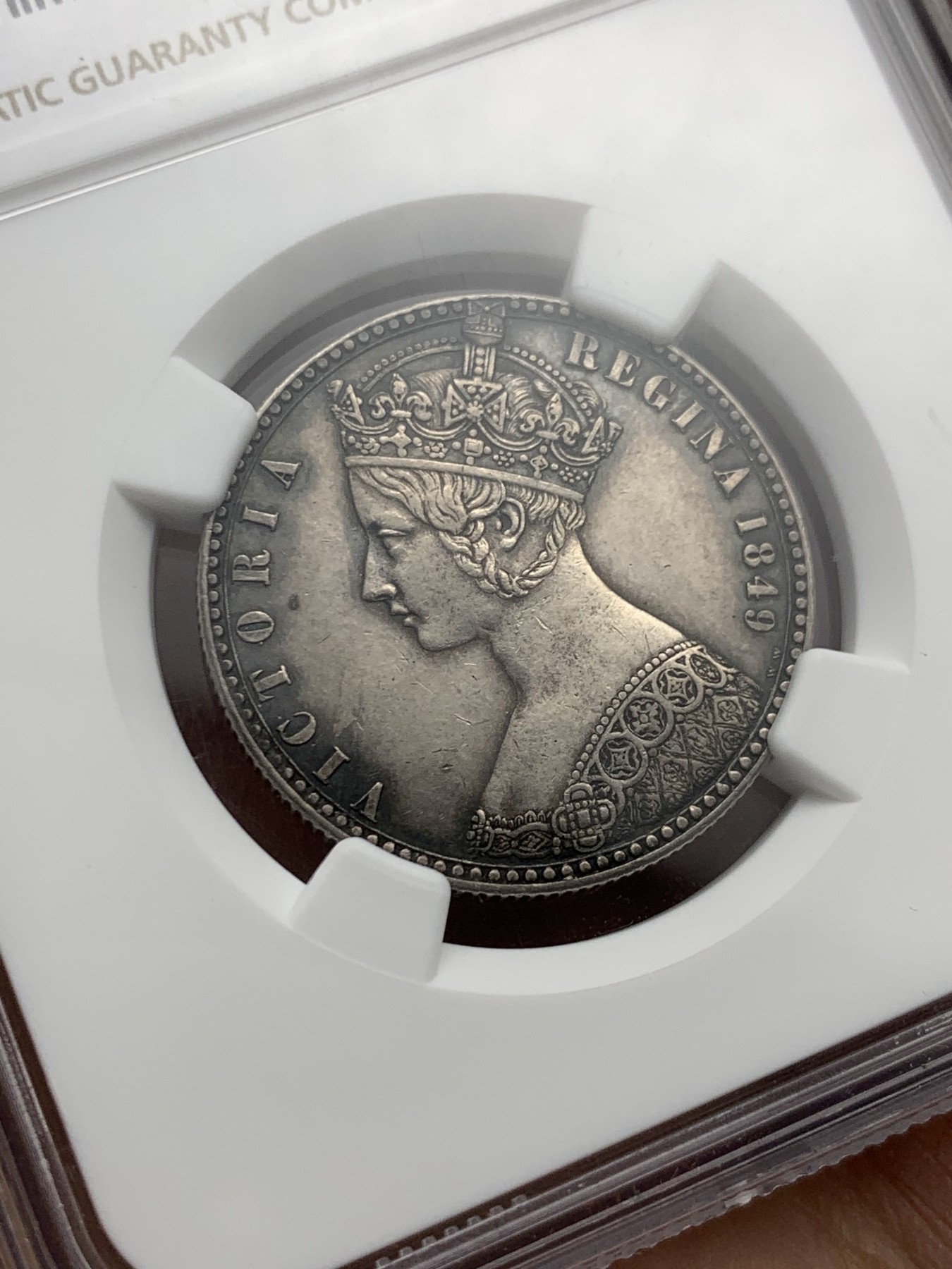 《竞宝斋》第240场-周日，周一 年终尾场 (全场包邮) NGC-AU55 英国1849年维多利亚无神弗洛林银币 英国第一枚弗洛林 第一枚没有D.G(君权神授) 正面是威廉怀恩作品 背面有代表英格兰、苏格兰、威尔士的三花 名誉品种 打制精美 五官皇冠服饰都清晰可见 特有的英系黑彩 钱币背后的故事丰富 只发行一年稀有（N家评级标签印成1949，难得的错误成了唯一）