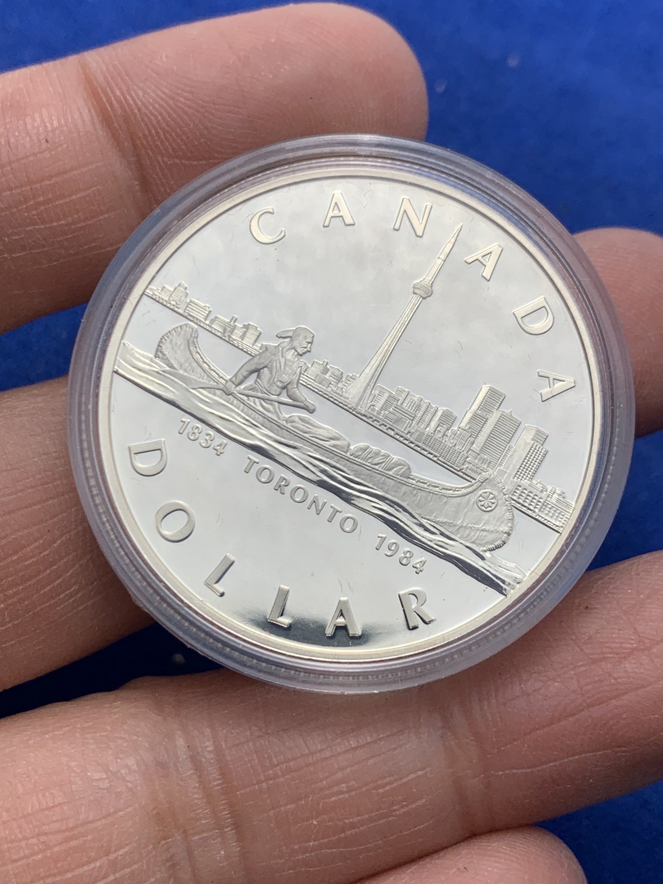 《竞宝斋》第247场-周日，周一 ，周二3场连拍 (全场包邮) 1984年加拿大多伦多市成立100周年纪念精制银币，直径36mm ，重23.3g 。正面为伊丽莎白二世女王年轻时右向胸像，背面为水面划船的印第安人背景为多伦多轮廓。全新原盒带证书镜面类精制银币，状态极佳。