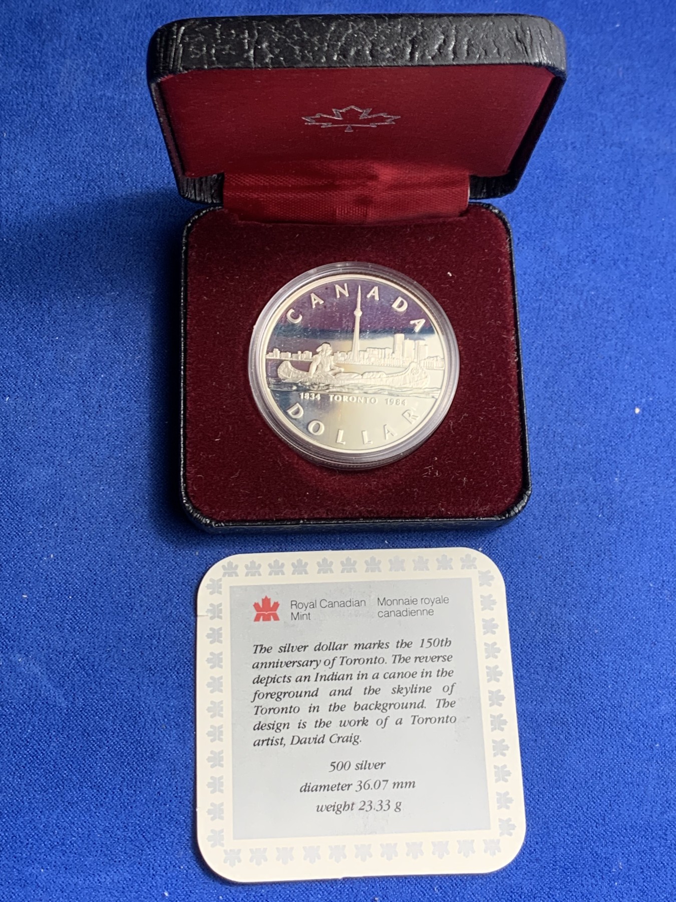 《竞宝斋》第247场-周日，周一 ，周二3场连拍 (全场包邮) 1984年加拿大多伦多市成立100周年纪念精制银币，直径36mm ，重23.3g 。正面为伊丽莎白二世女王年轻时右向胸像，背面为水面划船的印第安人背景为多伦多轮廓。全新原盒带证书镜面类精制银币，状态极佳。