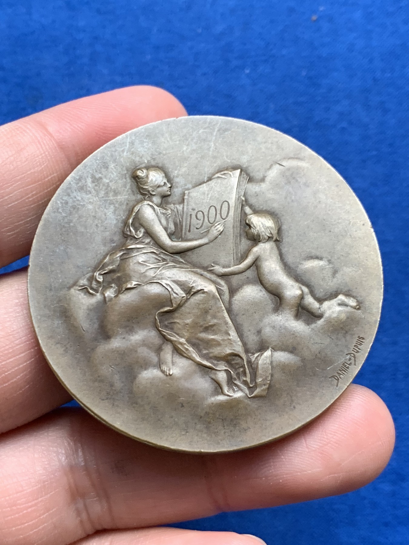 《竞宝斋》第261场-周日，周一，周二 3场连拍 (全场包邮) 法国章牌艺术大师丹尼尔·杜普伊Daniel Dupuis作品 巴黎造币厂1900年参展国际博览会设计雕刻的纪念章 直径50mm 重59.2克 丰饶角铜标 正面：主题为“历史记录（l'Histoire）”的场景 优雅女神手捧书卷 裙子随风轻盈摇曳 背面图案是压铸机 巴黎造币厂