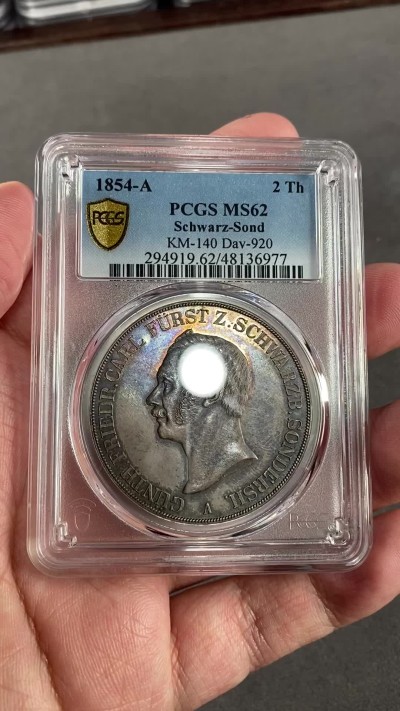 万国钱币拍卖第024期（诸神之战） PCGS MS62 1854年德国施瓦茨堡-桑德斯豪森野人2泰勒 可能是所有德国币爱好者都想拥有的品种，堪称德邦时期2泰勒的代表之作，独特的纹章设计令人过目难忘，无奈发行量少得可怜，留下的好品更是寥寥，注定只能流入少数藏家之手。此枚分数虽算不上顶级，但状态异常亮眼，双面醇厚的老五彩包浆和几乎无磨损的高点相得益彰，底板整洁无伤，绝对可堪入藏的一枚。