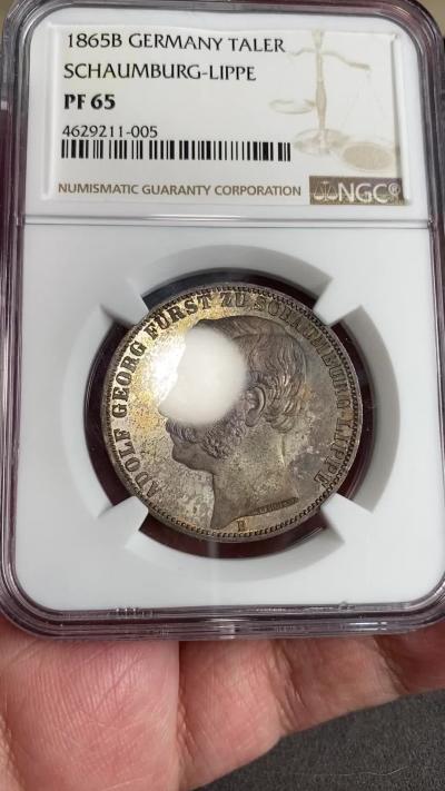 万国钱币拍卖第025期（槐月至·百币艳） NGC PF65 1865年德国绍姆堡·利普亲王国天使流通精制泰勒 堪称德意志邦国时期设计最为精美的纹章，其铸造工艺也是顶级， 镜面五彩让人爱不释手，外拍好状态裸币很多都在1.5W以上，能出65分的概率微乎其微，珍惜国内捡大漏机会。