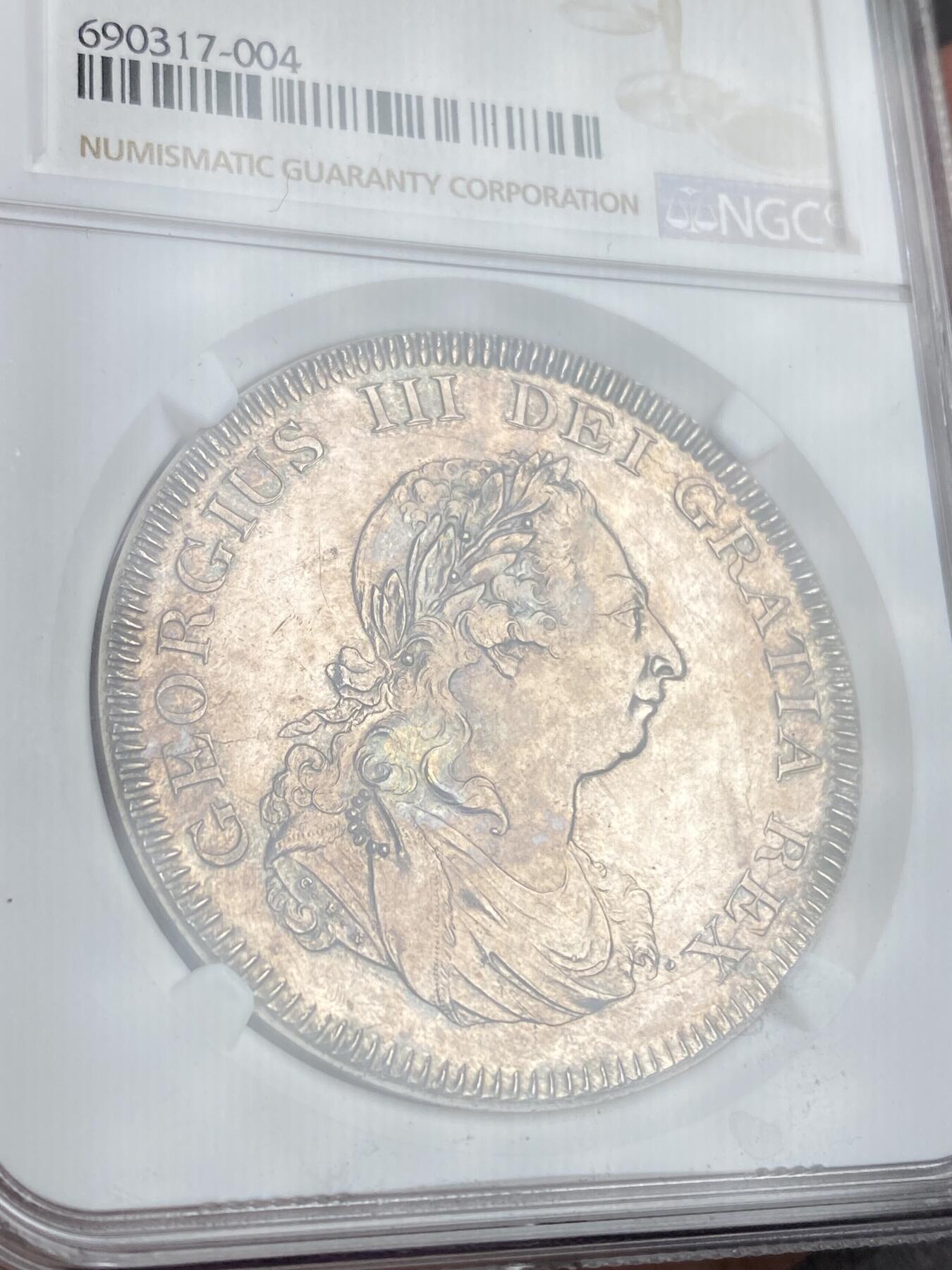 【麦稀奇世界钱币展】万国钱币拍卖第027期（五月端阳●万国夏季大拍） NGC MS62 1804英国乔治三世5先令大银 SOHO造币厂出品，直接压印在西班牙人像双柱上，还能依稀看到一些西班牙双柱的痕迹，非常有意思的品种，好品也并不多见，此枚压印完整，细节完好，正面淡金，背面蓝灰，值得出手的一枚。