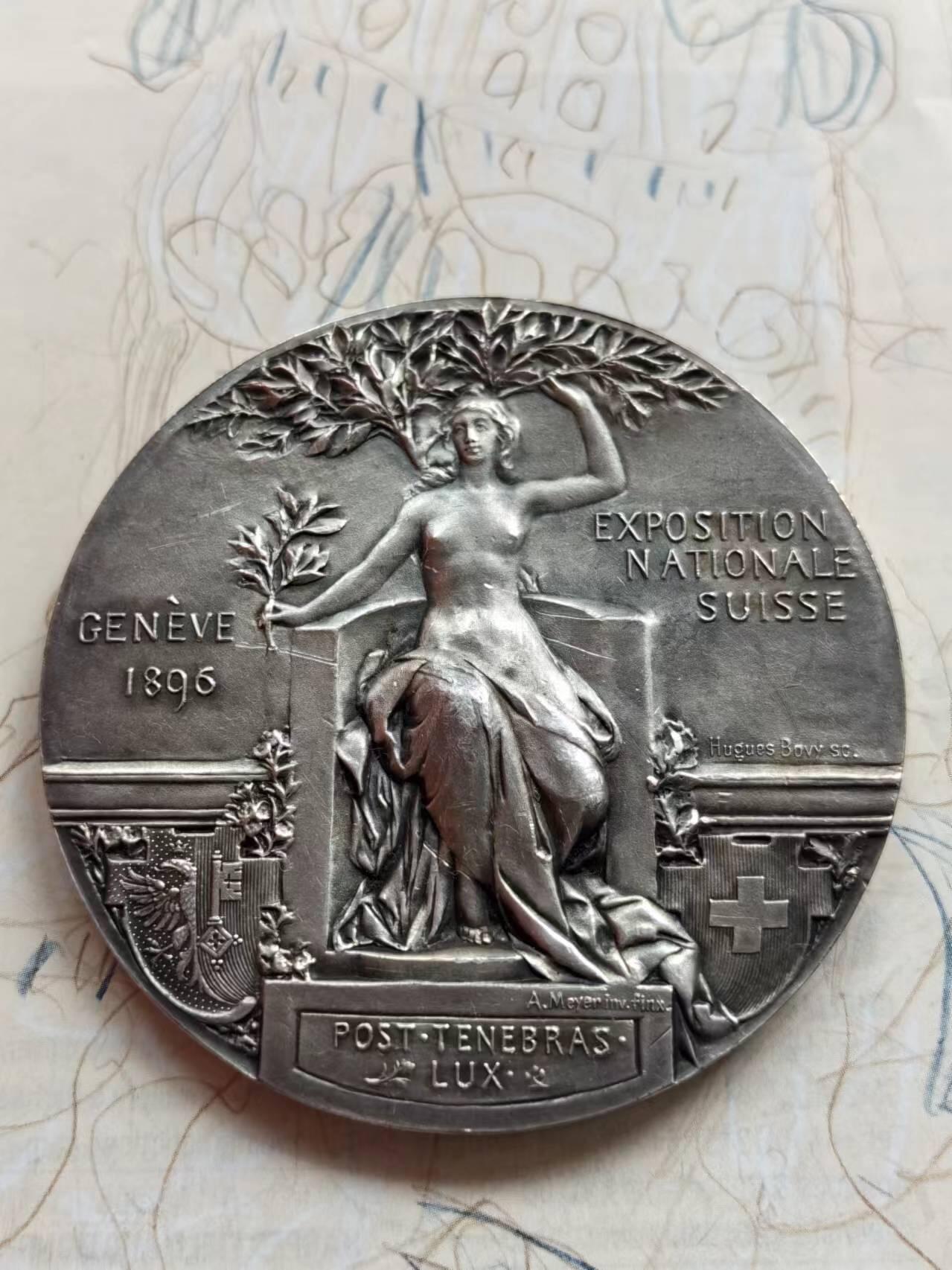 麦稀奇世界钱币展精品章牌第二十四期 1898年瑞士银章，日内瓦博览会，62mm，124g。 本例是难得的瑞士大尺寸银章。1898年日内瓦展览是19世纪瑞士举办的规模最大的展览会，同时举办的还有各种射击比赛