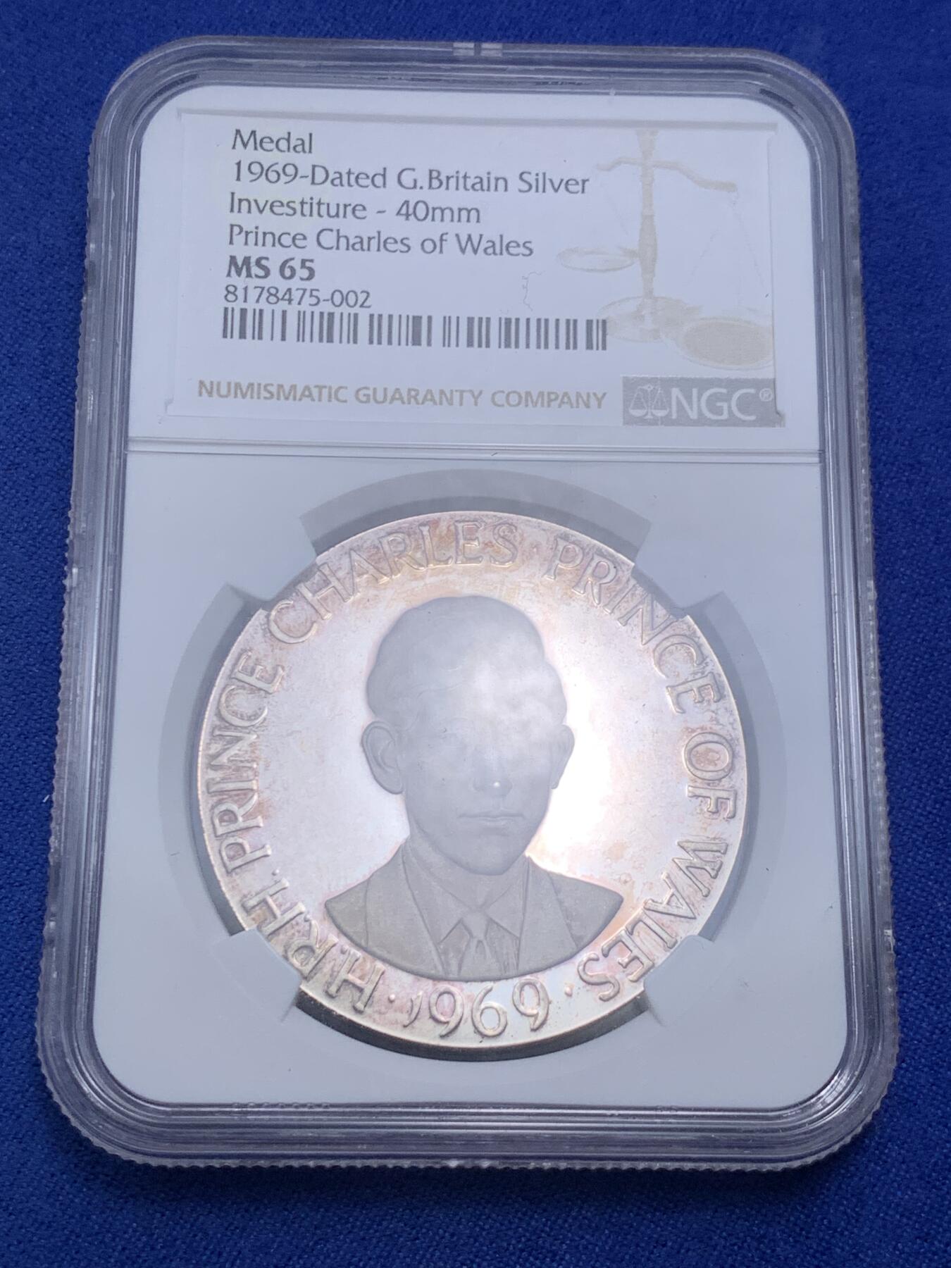 《竞宝斋》第280场- 周日，周一 ，周二3场连拍 （全场包邮） NGC MS65 英国1969年 查尔斯王子 威尔士亲王 银章 卡那封自治市69届展览亲王到访，重1盎司33.5克，纯度99.9%，自然氧化呈献了橘色的包浆，双面深度镜面凝霜，且有着高浮雕的艺术表现。边铭编号1712，发行量预计在小千枚，很少见。