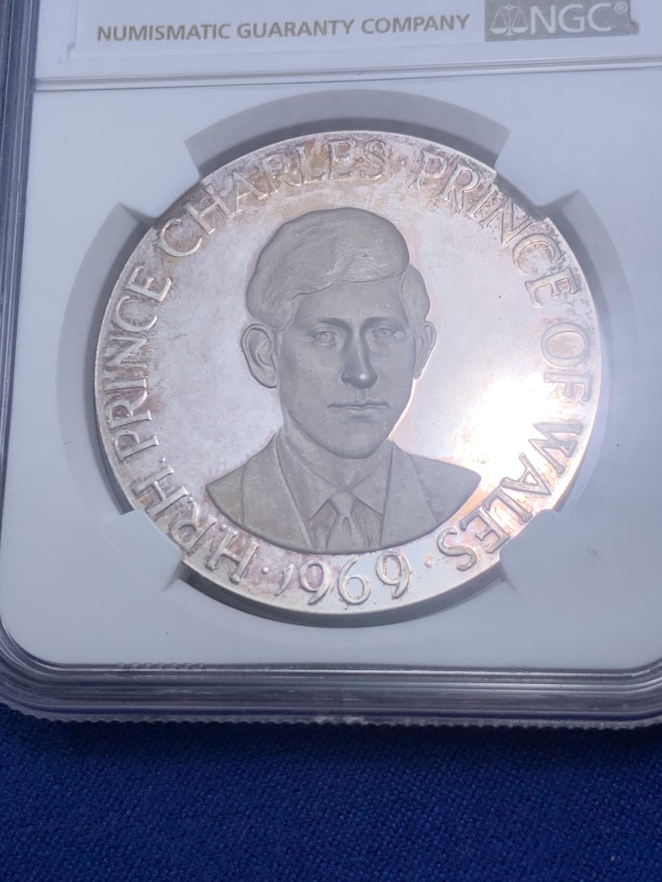 《竞宝斋》第280场- 周日，周一 ，周二3场连拍 （全场包邮） NGC MS65 英国1969年 查尔斯王子 威尔士亲王 银章 卡那封自治市69届展览亲王到访，重1盎司33.5克，纯度99.9%，自然氧化呈献了橘色的包浆，双面深度镜面凝霜，且有着高浮雕的艺术表现。边铭编号1712，发行量预计在小千枚，很少见。