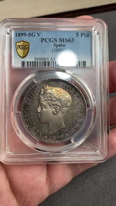 万国钱币拍卖第028期（花前月下●同享良章美币） PCGS MS63 1899年西班牙5比塞塔大银币 经典男童设计，海格力斯双柱。通体原味虹彩包浆，车轮光打制优异底板佳。实物非常漂亮，远超白板的视觉享受，也没有一般63的伤痕累累。评分略微保守，作为流通币保存状态相当不错。相对少见的年份，值得收藏的热门西班牙大银。