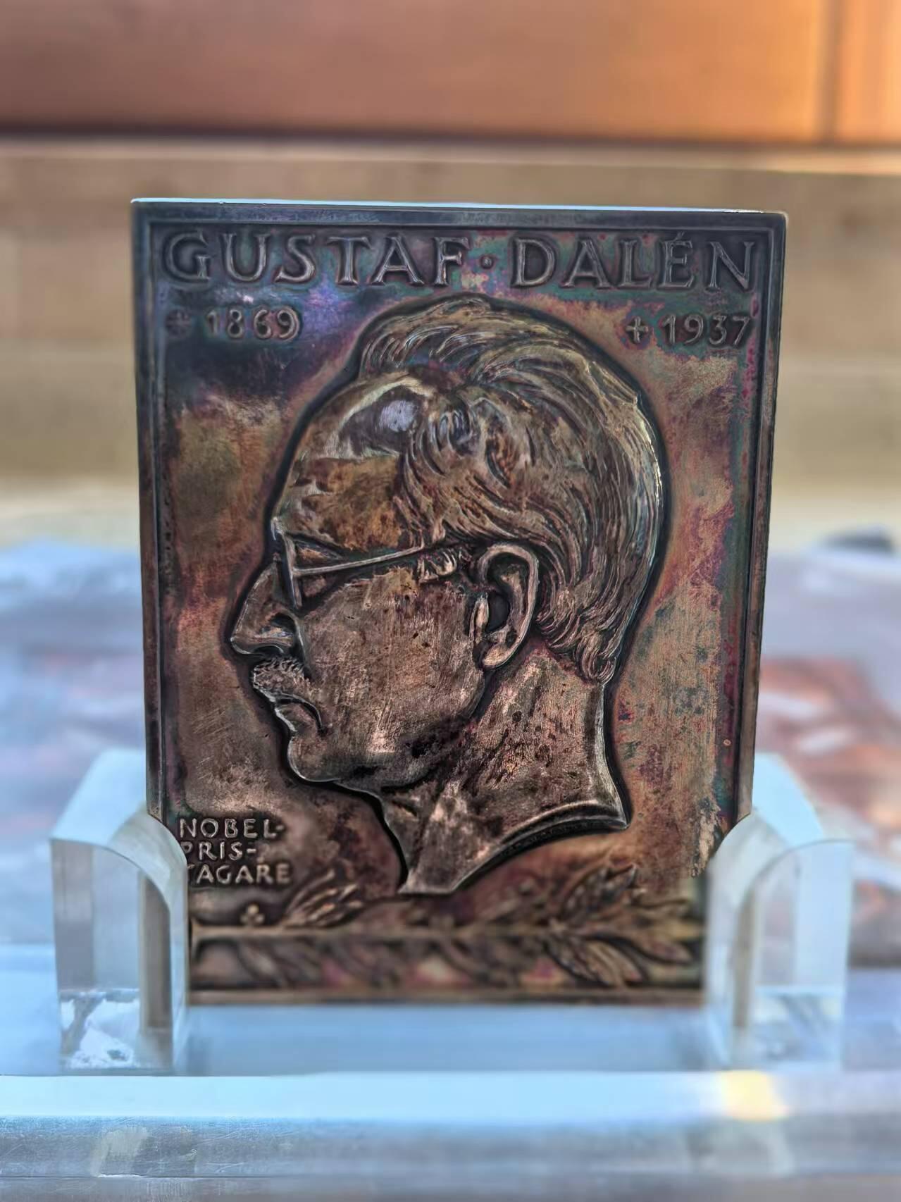 外国币章第二十五期 瑞典银章，5.5x7.5 cm，126g。Gustaf Dalén，1869年11月30日-1937年12月9日)，瑞典物理学家与发明家，研究领域为机械工程的应用。1912年因为发明结合燃点航标、燃点浮标和蓄电池等功能的自动调节装置而获得诺贝尔物理学奖。 本章正面是他的半身像，背面寓意他发现的光明照亮了地球。自带特制亚克力摆架，彩色包浆。