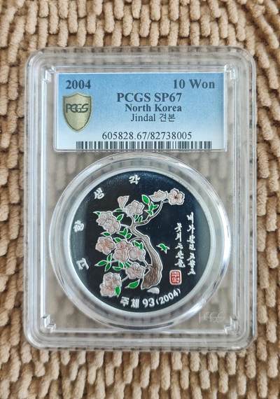 10月18日 币章（罕珍稀） - 珍品：朝鲜 2004年版《思念故乡-金达莱花盼望朝鲜半岛统一图》纪念币 彩色精制铝样币 PCGS 67分