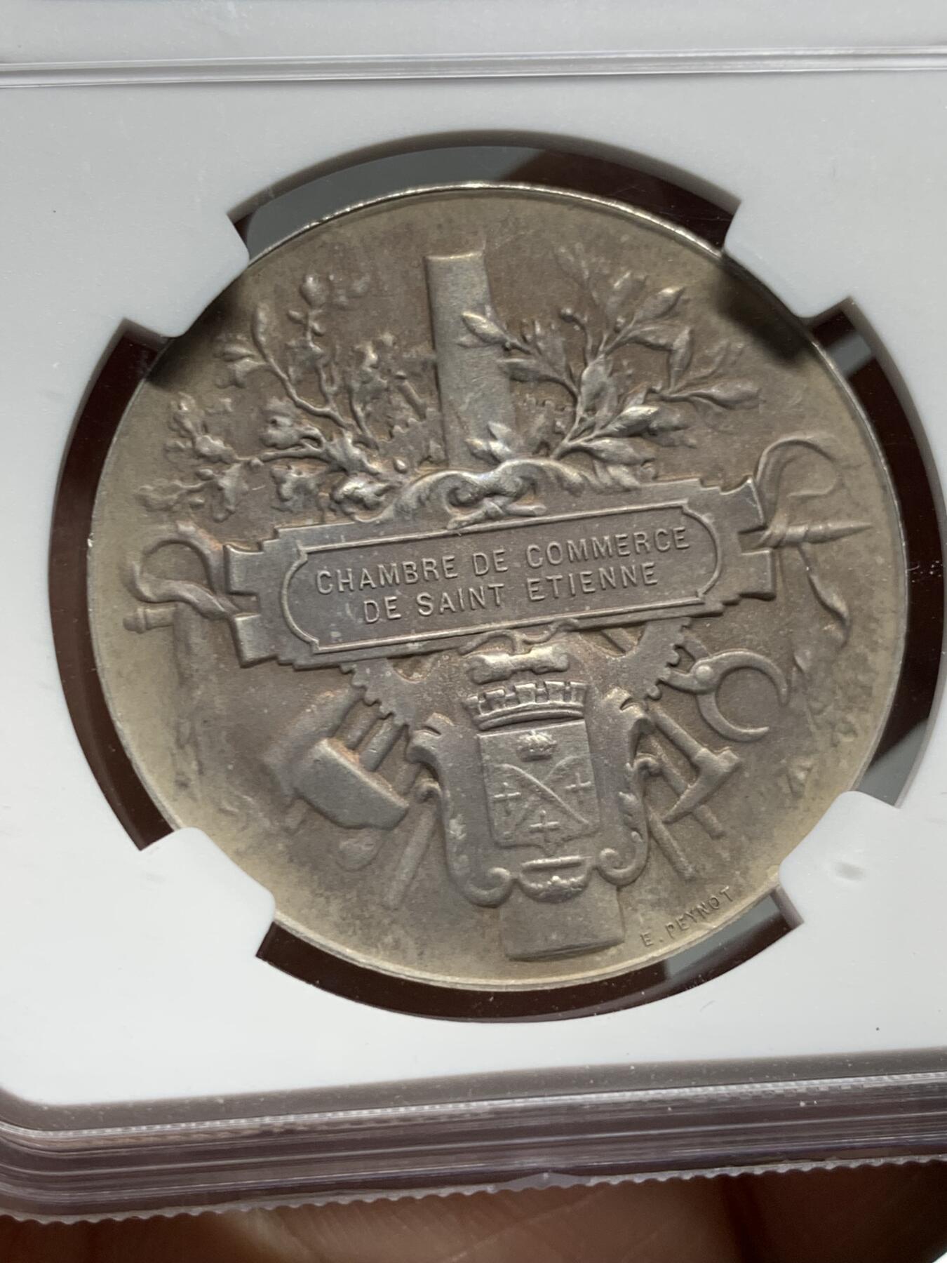 《竞宝斋》第339场 周日，周一，周二 3场连拍 （全场包邮） NGC MS63 少见银质奖章。法国圣艾蒂安商会奖章。正面:矿工妻子，脚下一盏矿工灯，矿工坐在铁砧上，底部签名：E.PEYNOT 反面:锻造和采矿工具装饰