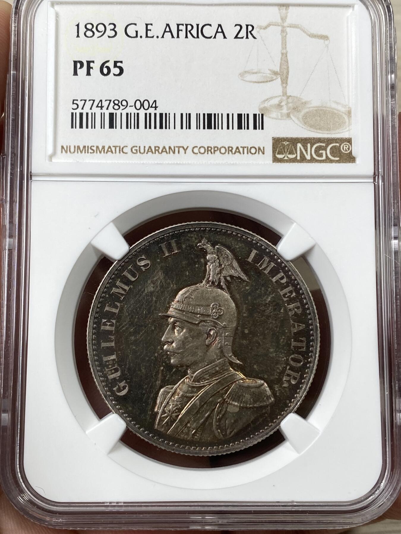 万国钱币拍卖第040期（万国2025新年大拍） NGC PF65 1893年德属东非威廉二世精制2卢比大银币  德属大名誉品种，德属东非领土总面积约为一百万平方公里，几乎是如今德国面积的三倍，普制高分已是难得一见，此等级别的精制已是另一个维度的存在，美到窒息的孔雀蓝彩，隔着盒子也能感受到其边齿的锋利程度，抛光镜面闪烁出的永恒之光让我们能一窥德意志帝国殖民时代的余晖，NGC唯一冠军。