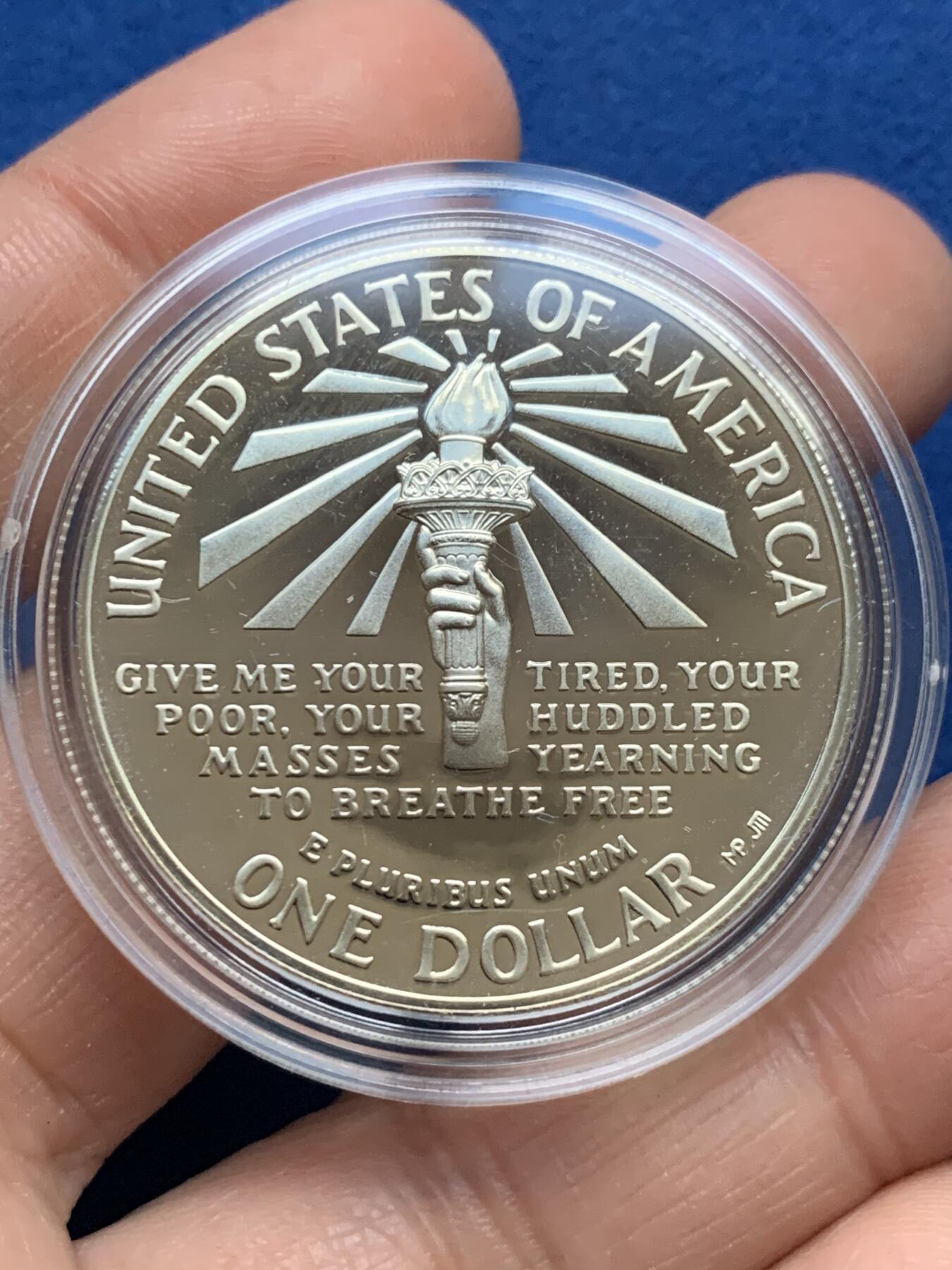 《竞宝斋》第353场 周日，周一，周二 3场连拍 （全场包邮） 美国1986年纪念自由女神像建成100周年精制银币套装。银币正面为庄严肃穆自由女神像，银币反面为自由女神像的火炬以及诗歌《新巨人》中的文字。 半美元铜镍币正面为纽约的天际线，自由女神像举起手臂，迎接一艘驶向纽约的班轮，太阳从东方升起，寓意着新世界新生活的开始。背面图案源自埃利斯岛上等待前往纽约的移民照片，反映了自由女神像作为移民希望象征的意义。