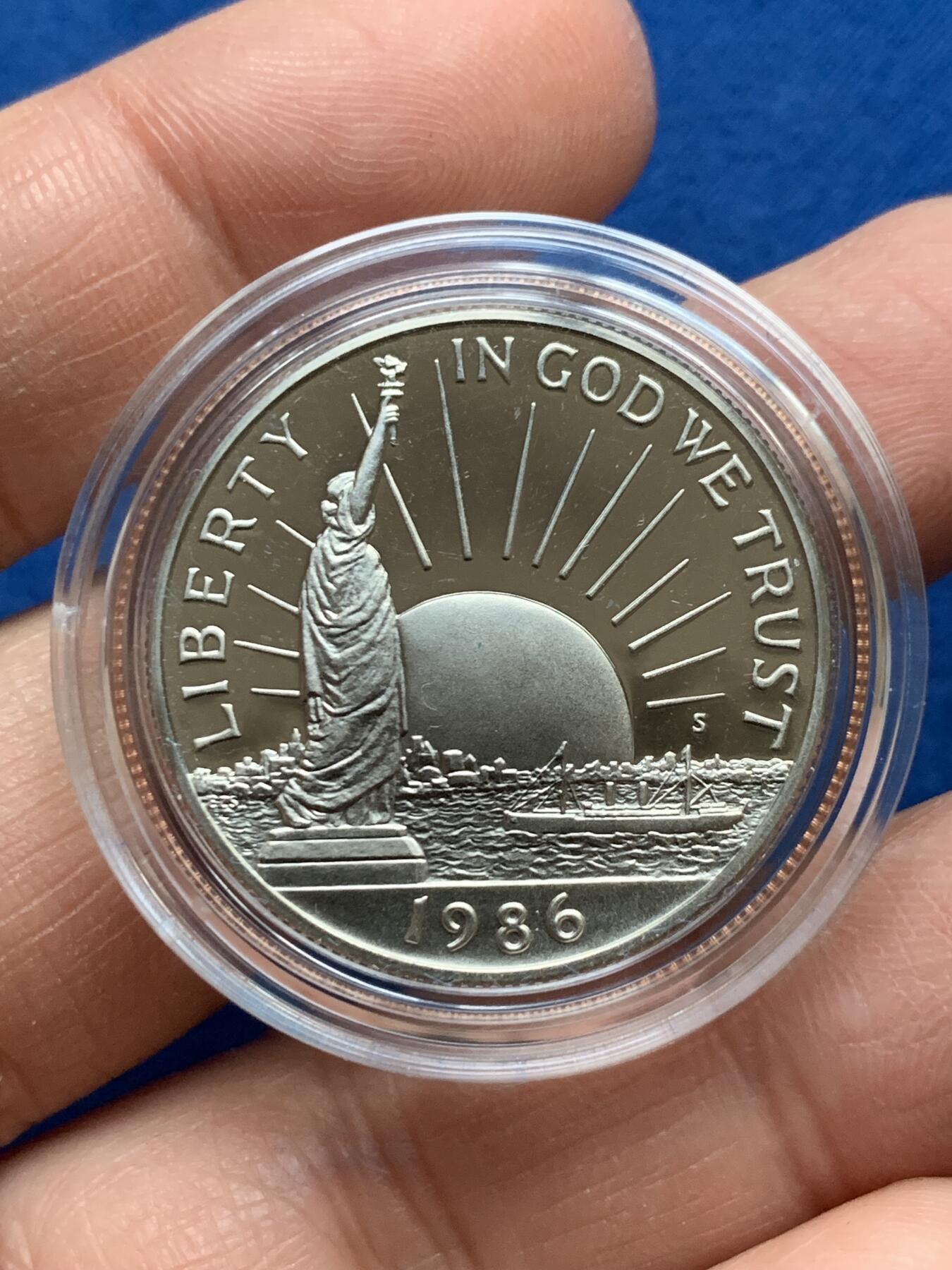 《竞宝斋》第353场 周日，周一，周二 3场连拍 （全场包邮） 美国1986年纪念自由女神像建成100周年精制银币套装。银币正面为庄严肃穆自由女神像，银币反面为自由女神像的火炬以及诗歌《新巨人》中的文字。 半美元铜镍币正面为纽约的天际线，自由女神像举起手臂，迎接一艘驶向纽约的班轮，太阳从东方升起，寓意着新世界新生活的开始。背面图案源自埃利斯岛上等待前往纽约的移民照片，反映了自由女神像作为移民希望象征的意义。