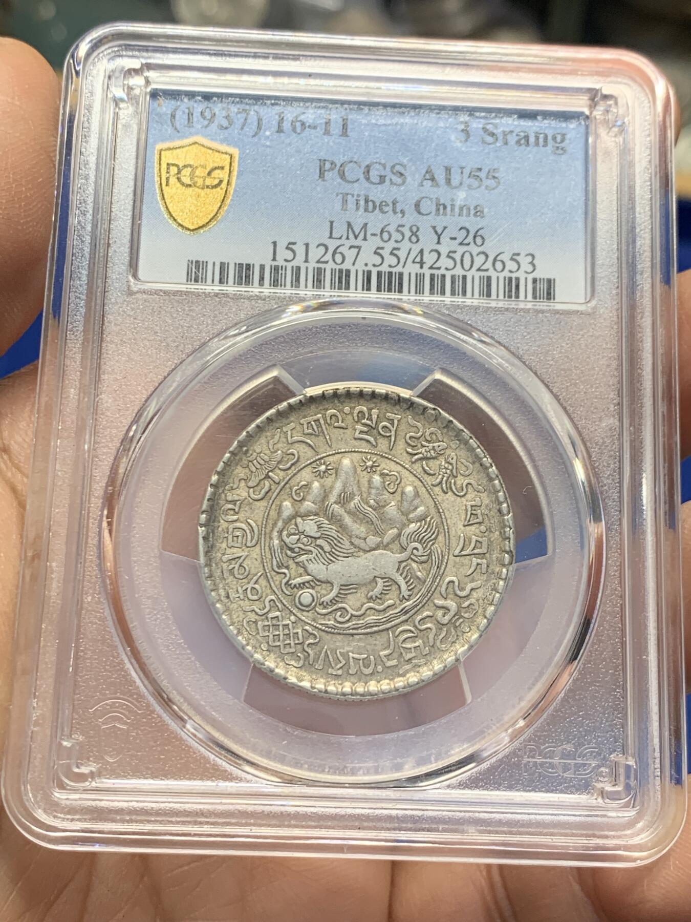 《竞宝斋》第353场 周日，周一，周二 3场连拍 （全场包邮） PCGS AU55 中国1937年西藏桑松果木三两银币，正面中央圆环内为日月、冈仁波齐雪山、祥云、狮子、绣球图案，外圈由宝伞（左上）、宝鱼（右上）、白海螺（右下）、吉祥结（左下）作为间隔环刻藏文“甘丹颇章，战胜四方”字样。背面中央圆环内为花枝和宝瓶图案，周围环绕缠枝纹和飘带；外圈以胜利幢（上）、金法轮（下）和莲花（左右）作为间隔，环刻藏文纪年、面值。具有独特的历史背景、文化内涵和艺术特征。此枚原味